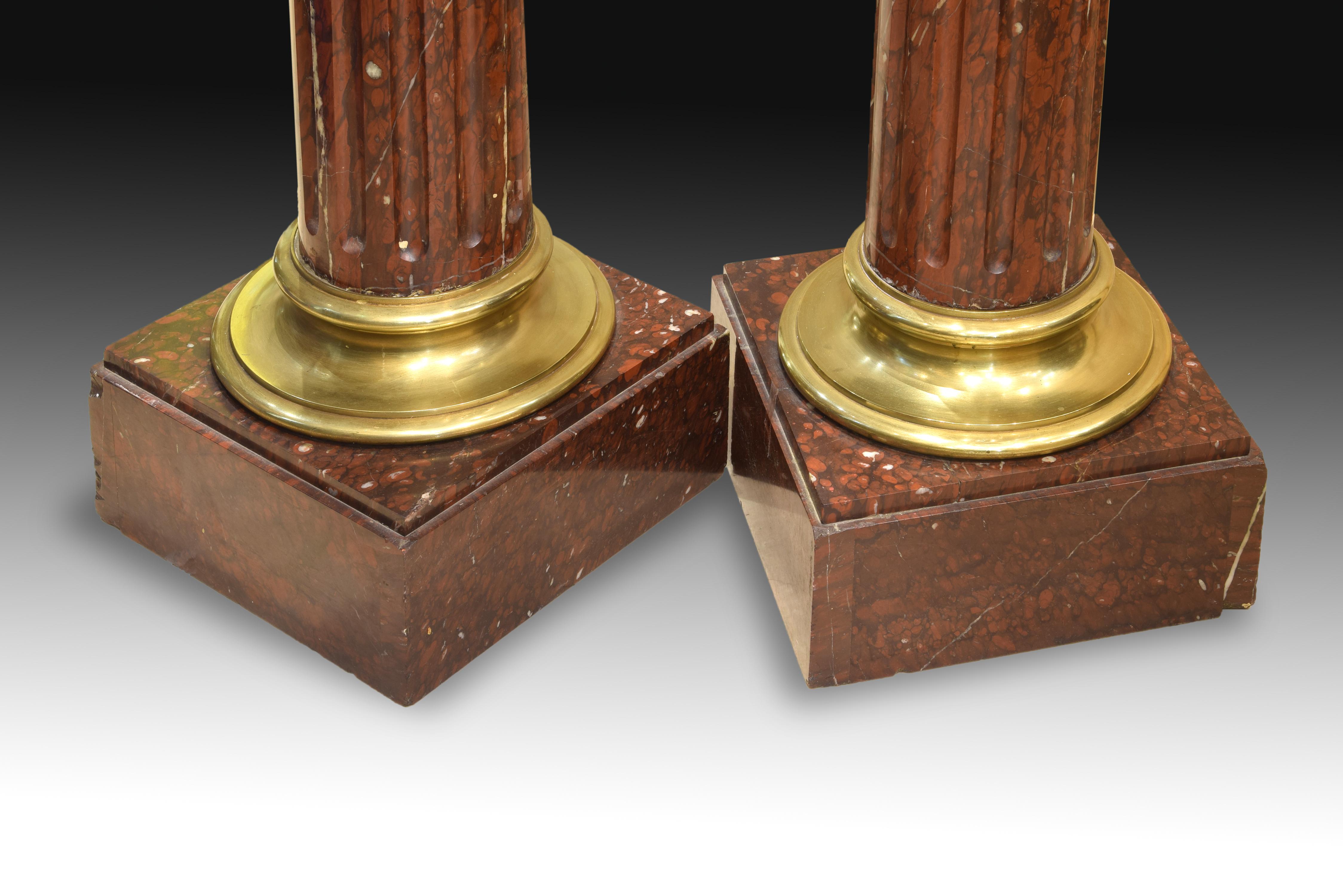 Pair of pedestals in the form of columns made of Rouge Griotte marble and gilt bronze, which have square bases and some tops in that same stone. Both practically the same, have a Tuscan-like capital on a concave molding, which is presented on top of