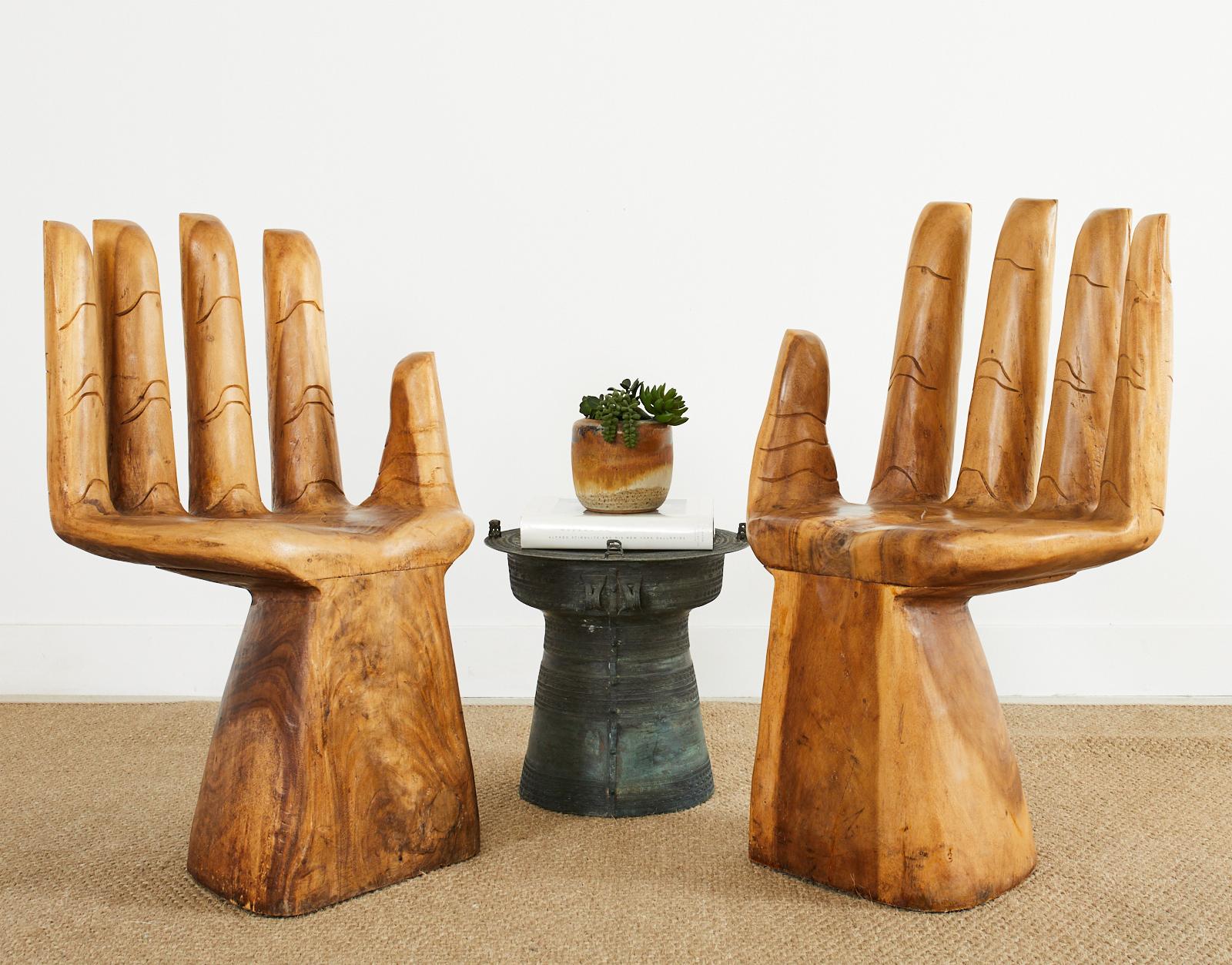 Sculptural pair of hardwood carved hand chairs made in the iconic manner and style of Pedro Friedeberg (Mexican b. 1936). The outside of the chairs have intricately carved nails and joints. The hands are mounted to heavy solid wood pedestal bases.