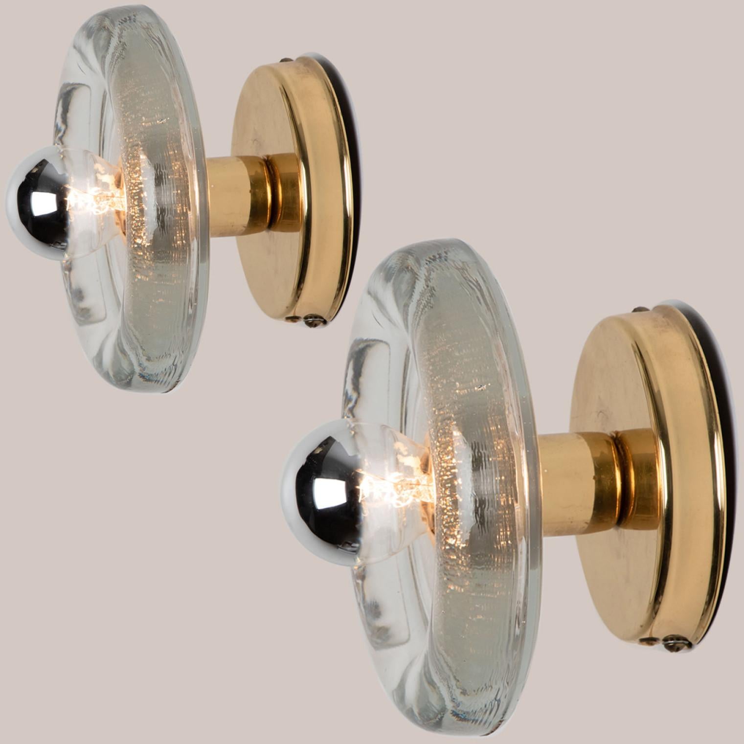 
A pair of Putzler wall light in sculptural glass on a round brass frame, circa 1970s, Germany. A clear design, with modern materials.

This modernist design is focused on the textured round thick glass glass, when illuminated and with use of mirror