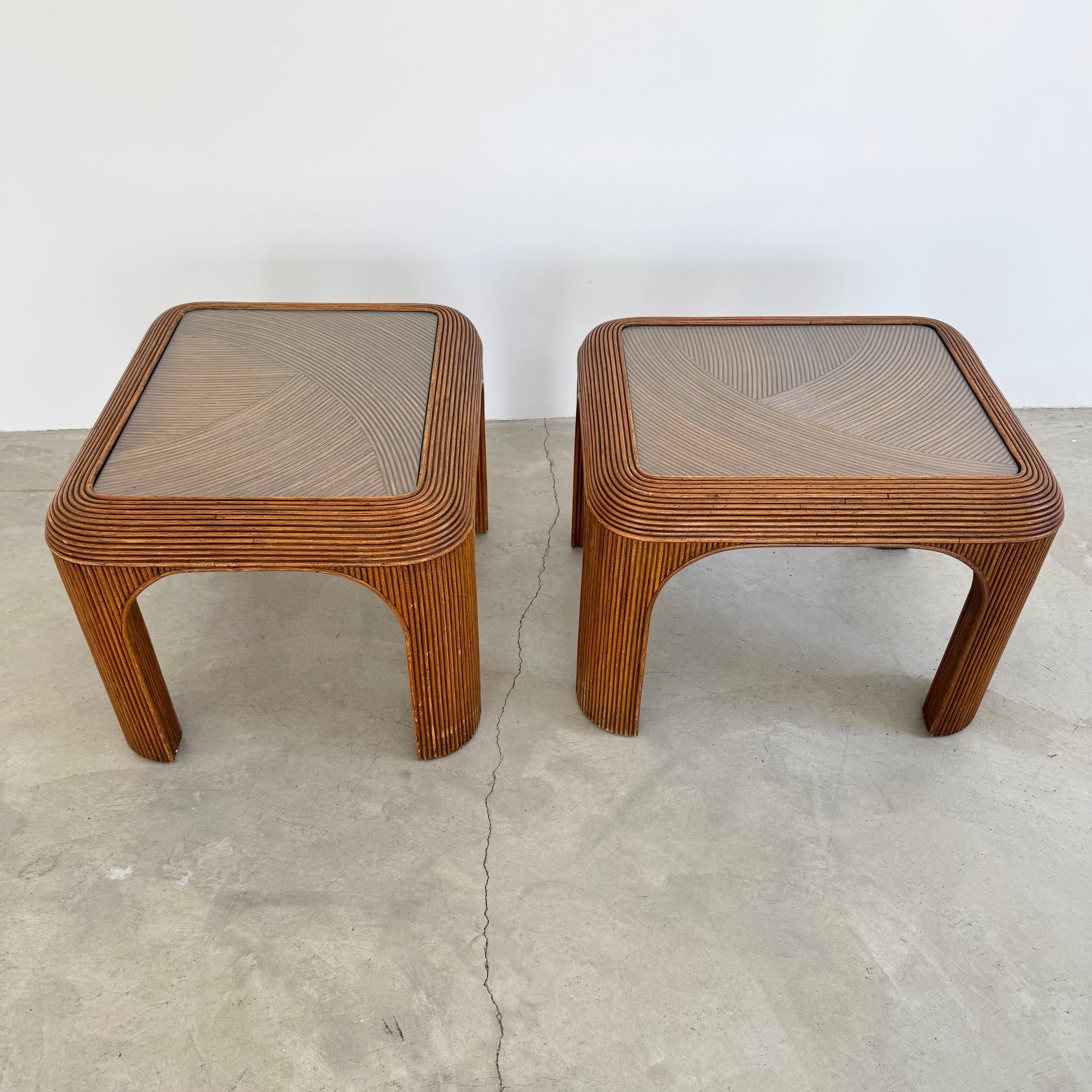 A chic pair of matching vintage pencil reed side tables, showcasing the natural warmth and texture of rattan craftsmanship. Each table features a square top with an inlaid geometric pattern beneath glass. The waterfall-style legs give the pieces a
