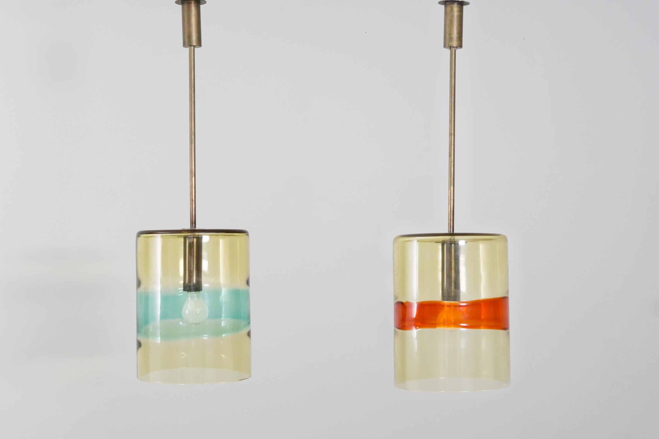 Beautiful pairs of pendants by Flavio Poli, made of hand blown glass with a light green tint and colored stripes in orange and turquoise. Brass mounting. Manufactured by Seguso Vetri D’Arte Murano. Originally part of the interior of Hotel Royal in