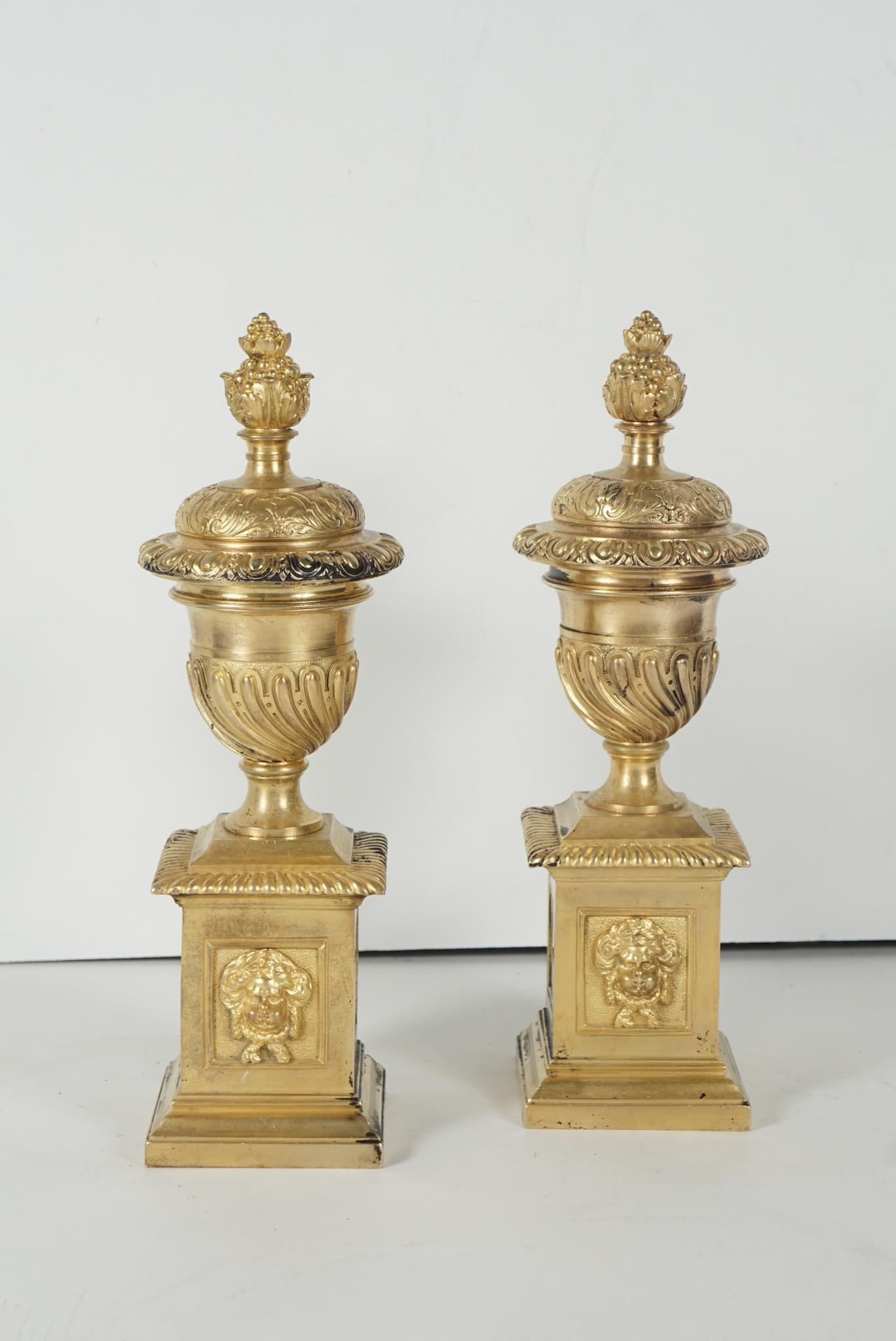 A pair of lovely small and well-cast English fire dogs, circa 1680-1700. Cast as urns resting on a raised plinth, the pair exhibit finely detailed attention in the chased raised decorative borders of historical patterns found in antiquity and