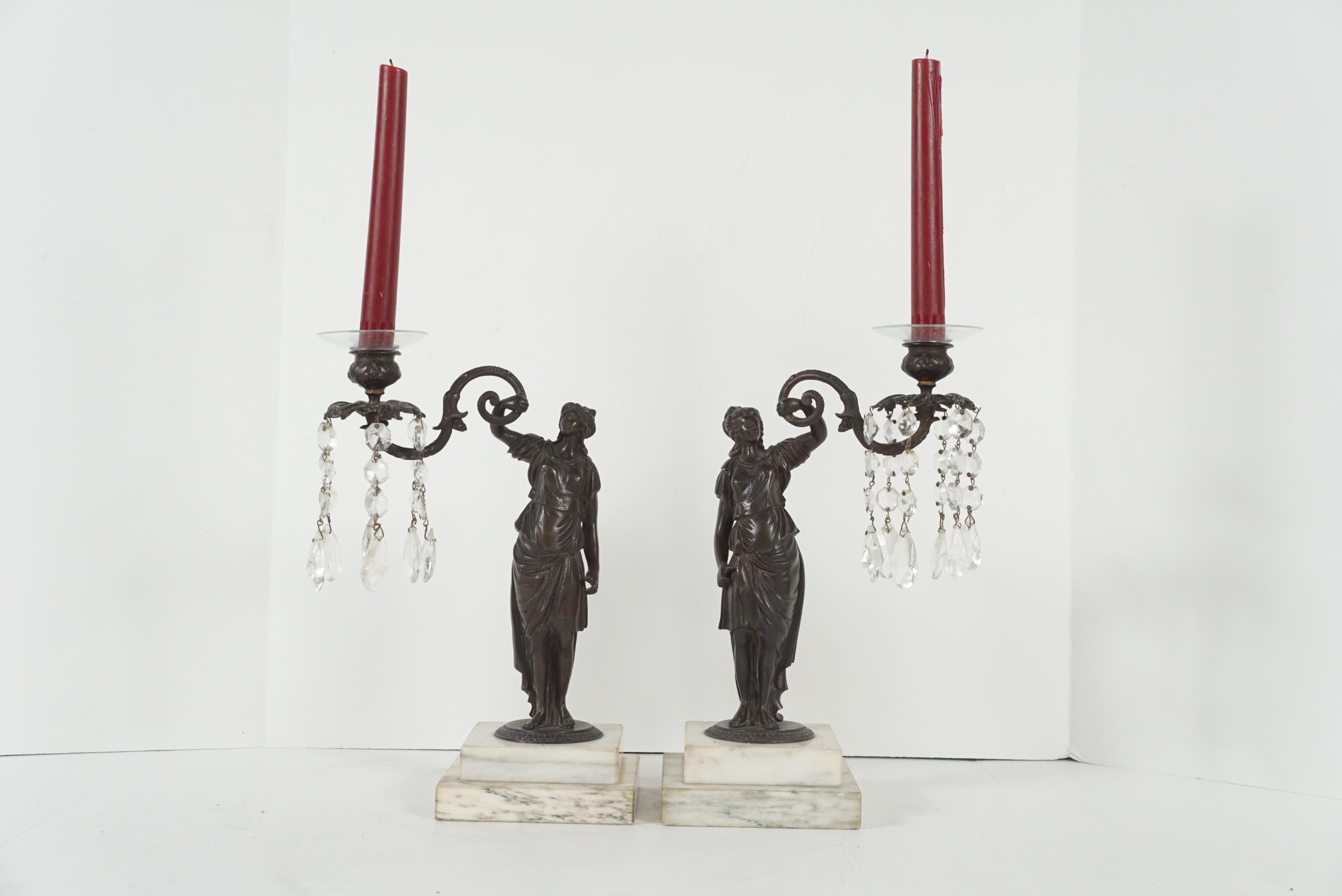 This pair of English candlesticks cast circa 1820 are made of bronze set on carved marble slab bases. The classically draped female figure in worked as opposing forms are well cast and with pleasing faces and forms. They hold in an outstretched hand