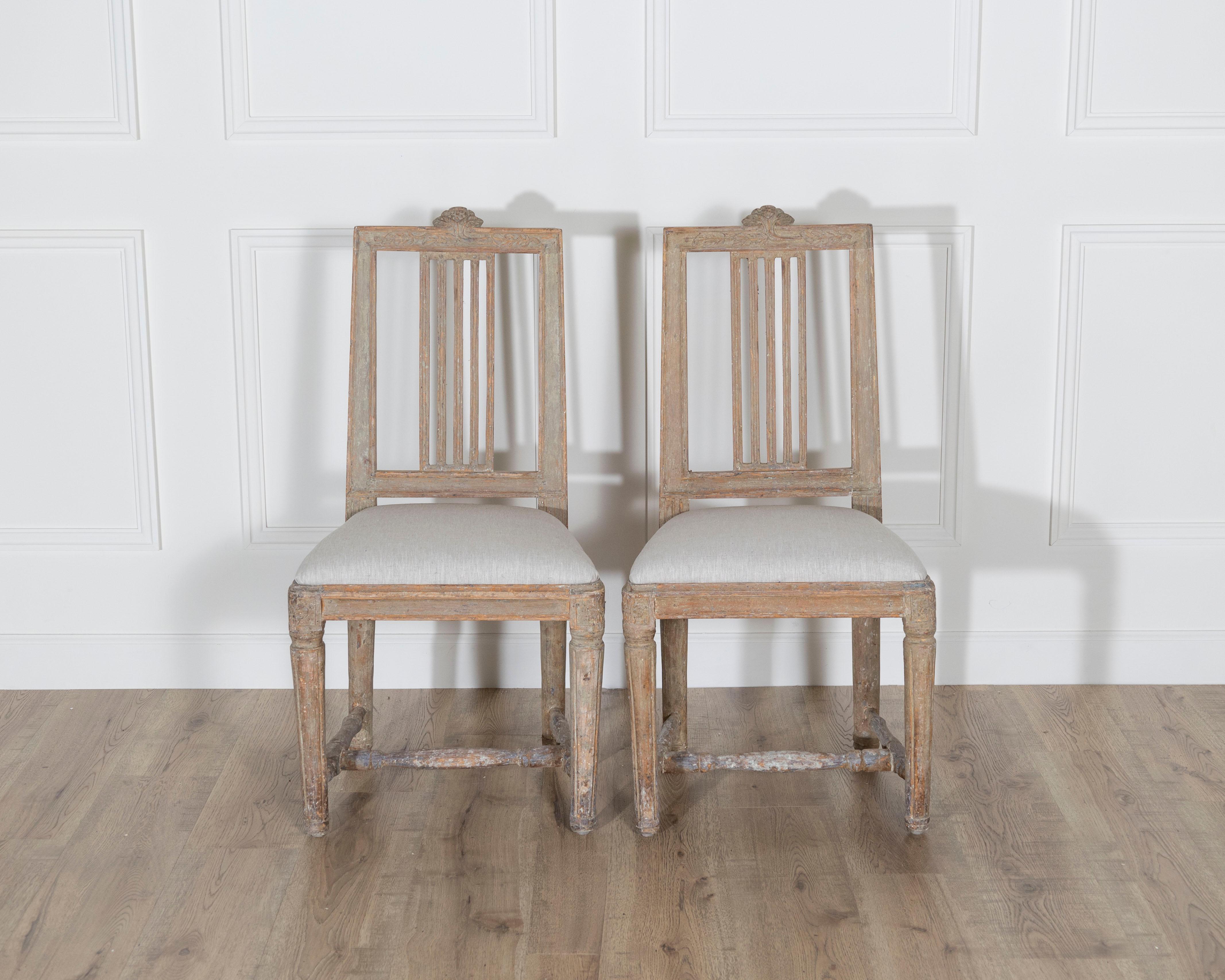 A charming pair of Swedish Gustavian side chairs from the late 18th century, each scraped back to reveal traces of their original soft grayish-white paint, now beautifully timeworn and evocative of their age. These chairs embody the restrained