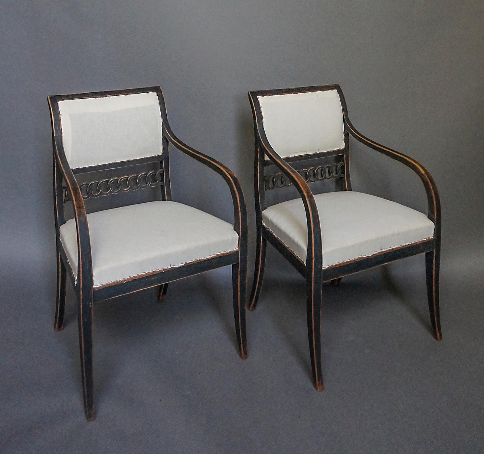 Pair of neoclassical armchairs, Sweden circa 1830, with later black paint. Square backs with a wide rail of interlocking rings below the upholstered panel. The curved arms extend down into the tapering saber legs. Graceful, sturdy and quite