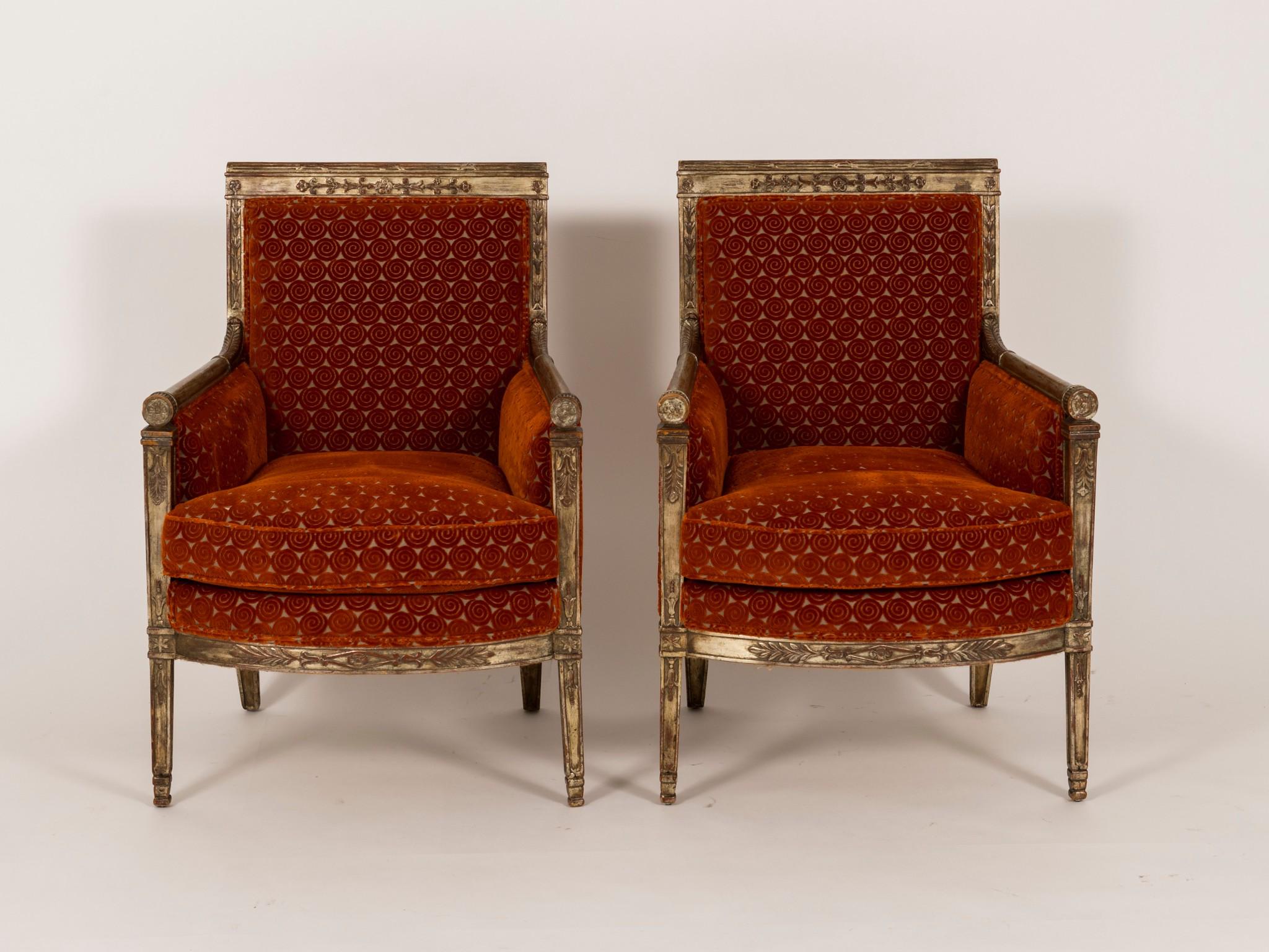 A pair of late 18th century French Directoire silver gilt bergères from a prominent San Francisco estate newly upholstered in a persimmon cut velvet with a lofty loose feather down cushion. These chairs have an array of wonderful detailed carvings.