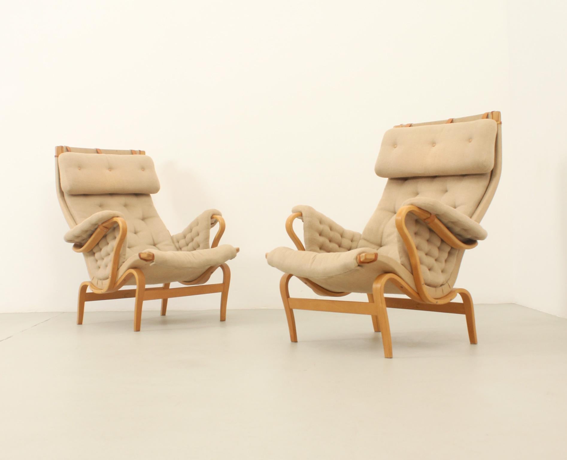 Pair of Pernilla armchairs designed in 1969 by Bruno Mathsson for Dux, Sweden. Curved beech wood structure with canvas, leather strips and original fabric. Signed. 