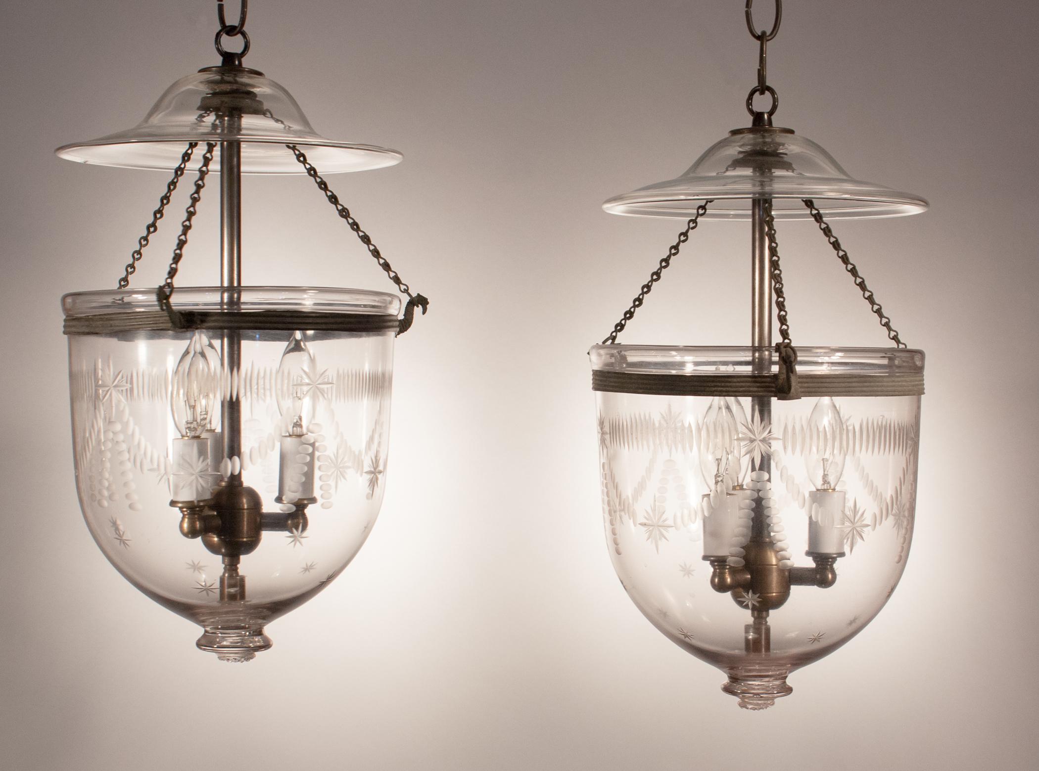 A charming, well-matched pair of antique hand blown glass bell jar lanterns with a Federal-style etching, original rolled brass bands and unusual chains. These petite pendant lights have been newly electrified with a three-bulb candelabra cluster