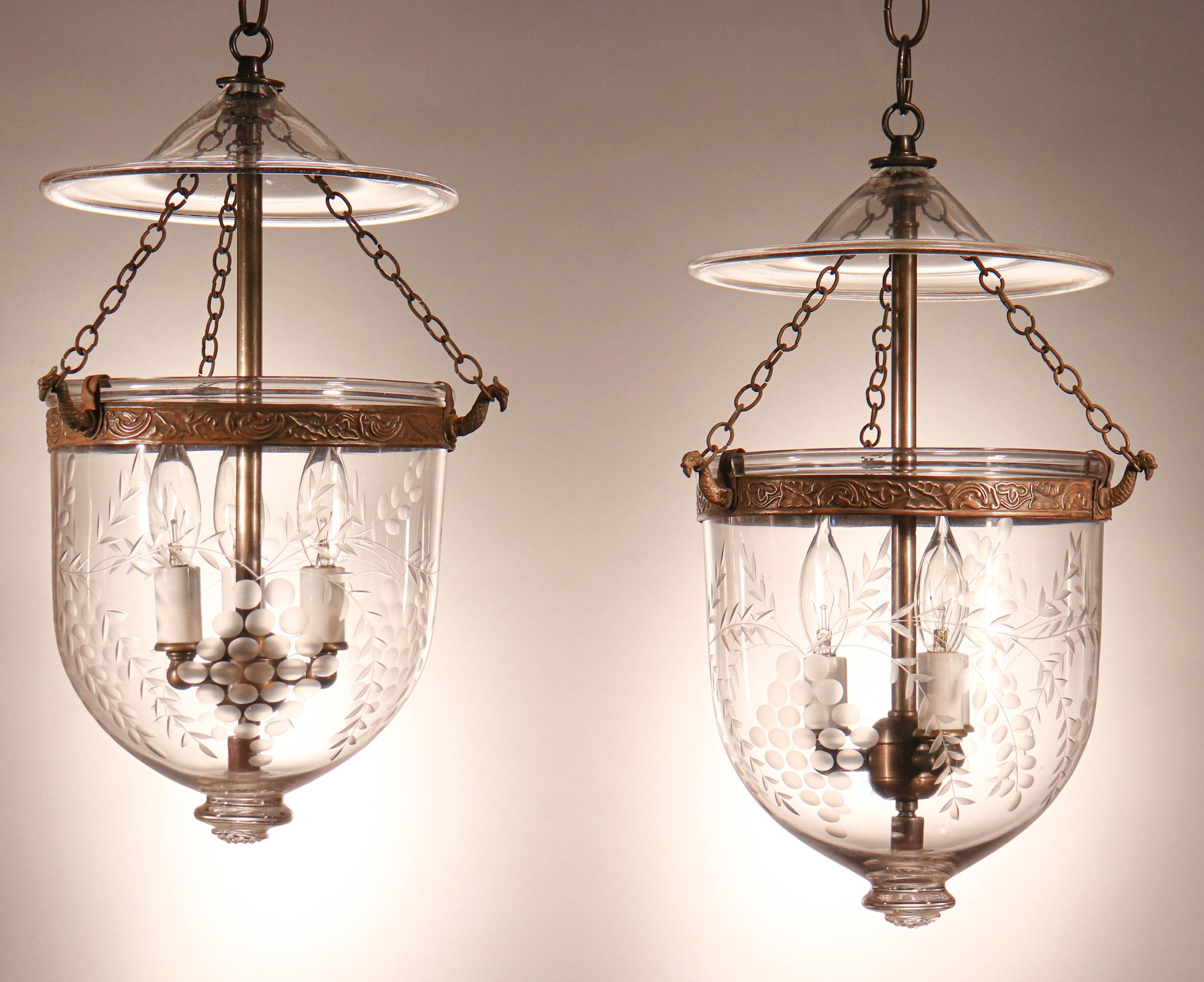 A lovely and well-matched pair of English hand blown glass bell jar lanterns with an etched grape motif. The embossed brass bands, which have a botanical design, have been replaced at some point to ensure that the pendants are secure when hanging.