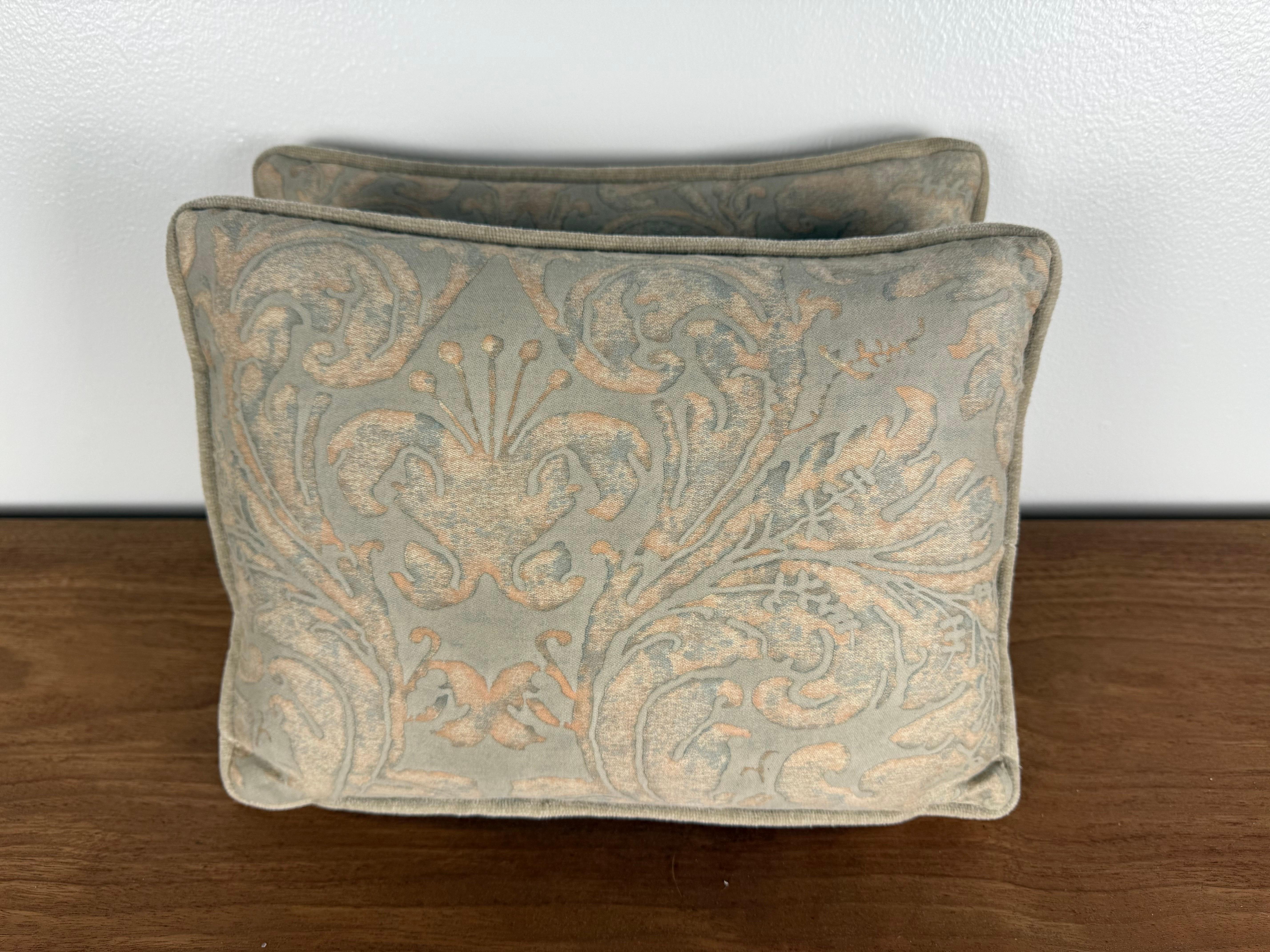 Una coppia di cuscini di dimensioni ridotte realizzati con l'autentico tessuto di Fortuny, che mette in mostra la maestria della casa nella stratificazione dei colori e nella lavorazione dei motivi. Il tessuto è caratterizzato da un morbido fondo