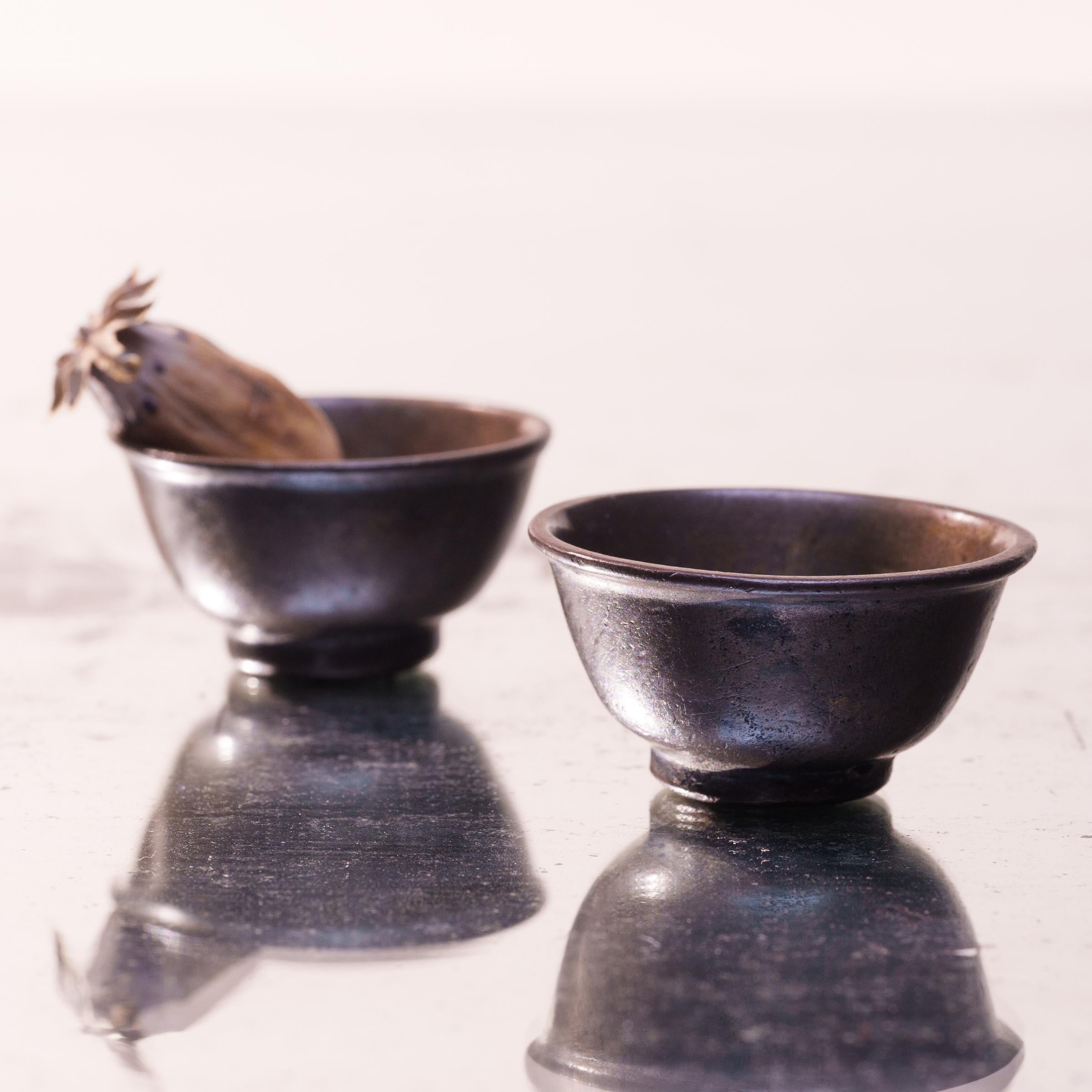 Minimal and refined, these petite bronze cups are simply formed with gently curved sides and a short footed base. The pair dates to the 19th century or earlier and would have been used for drinking tea, rice wine, or opium tea. The small cups are