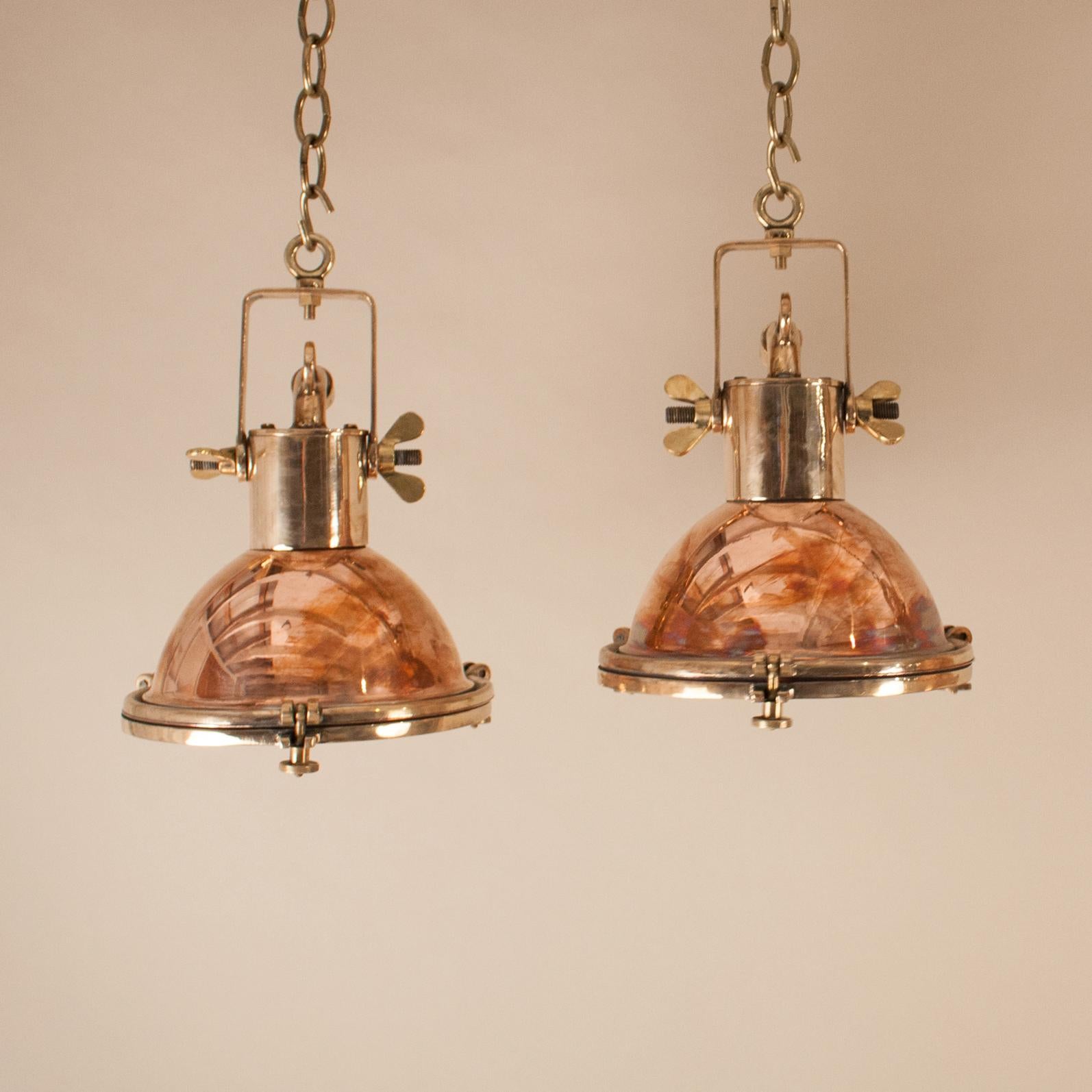 Pair of petite 1970s copper and brass ship passageway lights with nice proportion and patina. Salvaged from a maritime vessel and restored to near-original condition, these authentic Industrial pendants have interior reflectors and glass lenses. The