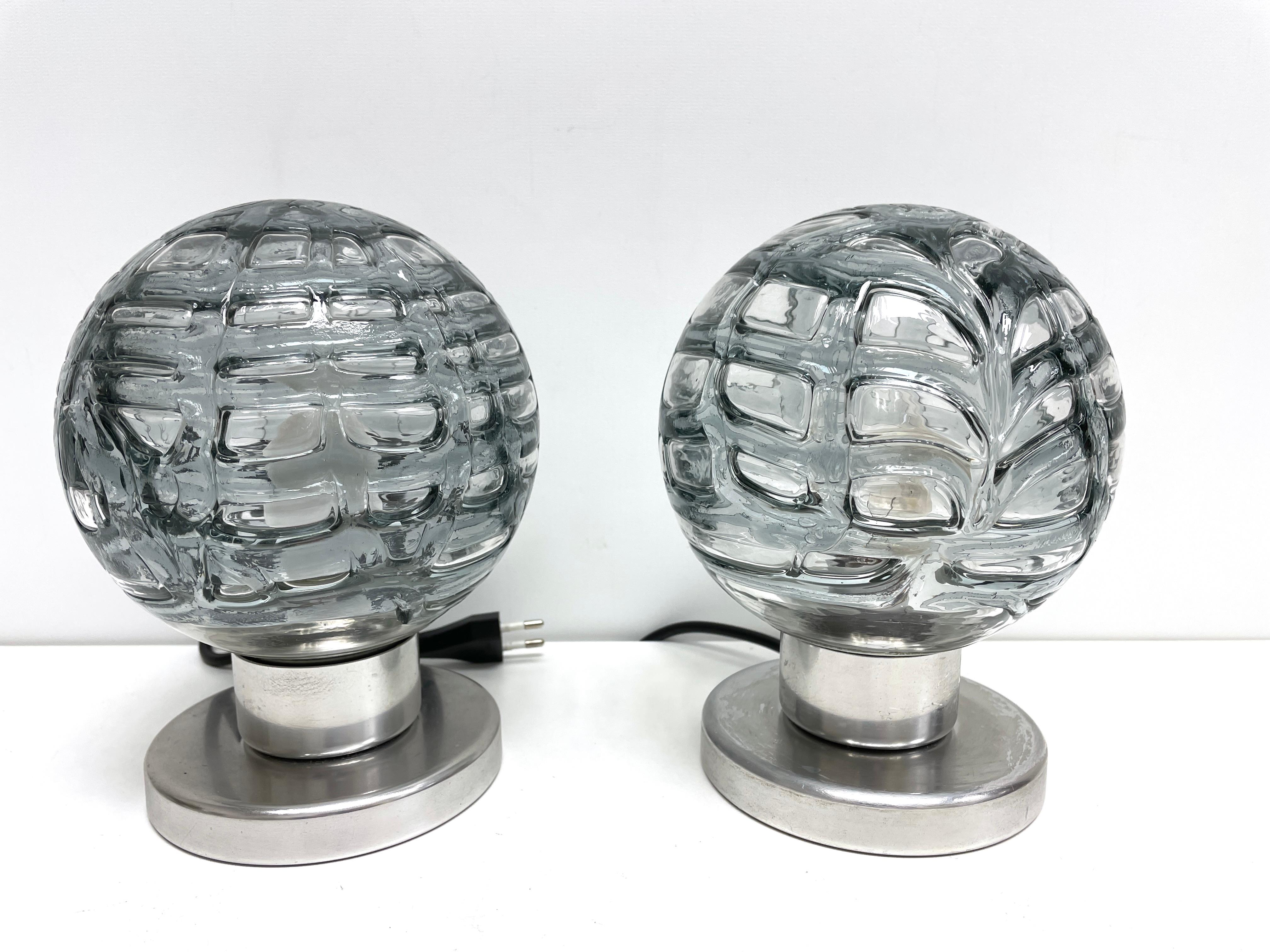 Kleines Paar Doria-Tischlampen aus der Jahrhundertmitte. Glas mit grau geräucherter Farbe. Sockel aus Aluminium. Jeder benötigt eine europäische E14 / 110 Volt Torpedo-Glühbirne, bis zu 60 Watt pro Stück. Wir können sie auch mit einem weißen