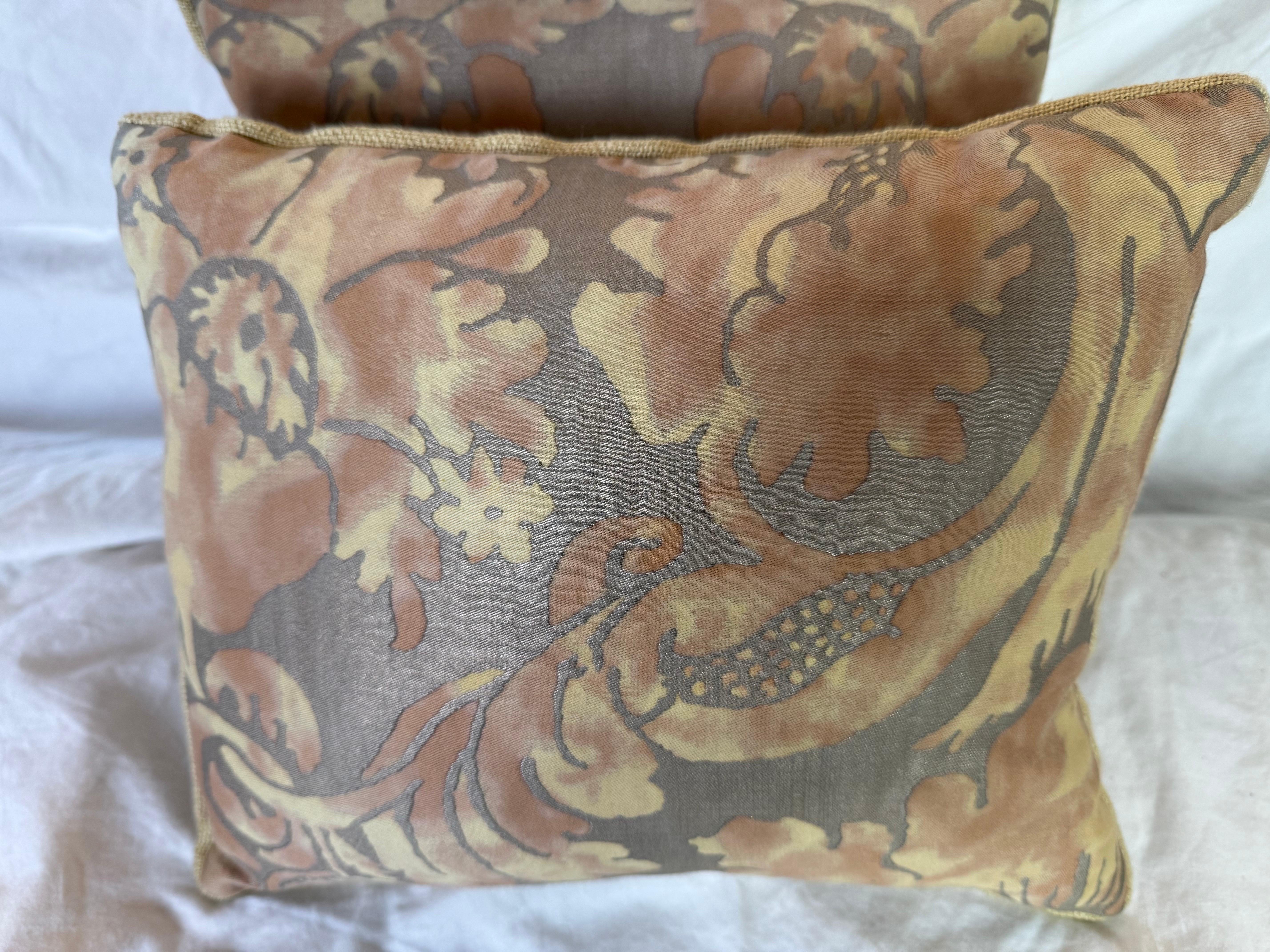 Cette magnifique paire de coussins est fabriquée à partir d'un textile authentique de Fortuny, présentant un motif floral et feuillu à grande échelle, rendu dans des tons chauds de terre cuite et d'ocre doré sur un fond taupe atténué. Le tissu de