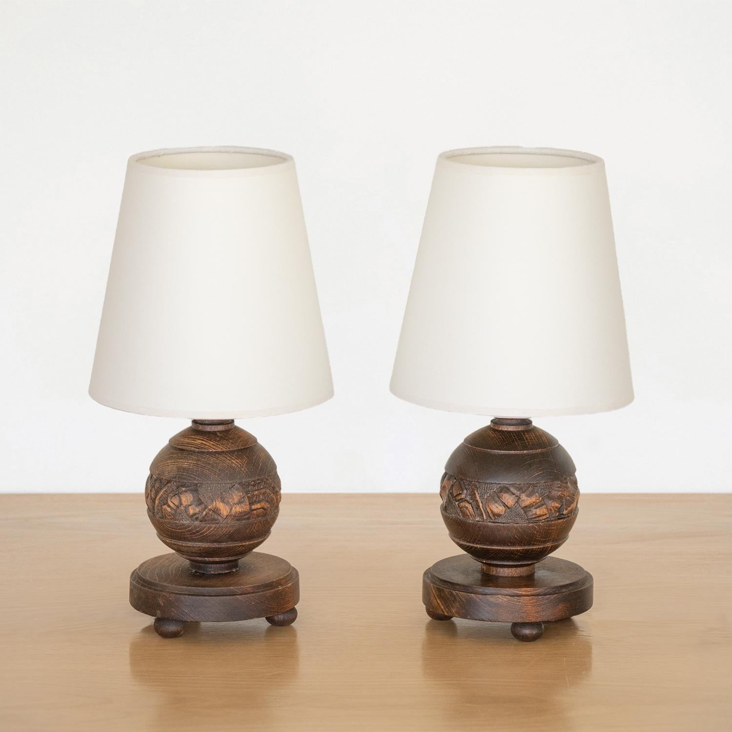 Pair of petite wood table lamps from France, 1940s. Carved wood ball forms with circular base and three petite wood ball feet. Original wood finish with beautiful carved floral detail. New tapered paper shades and newly re-wired. Each takes one E12