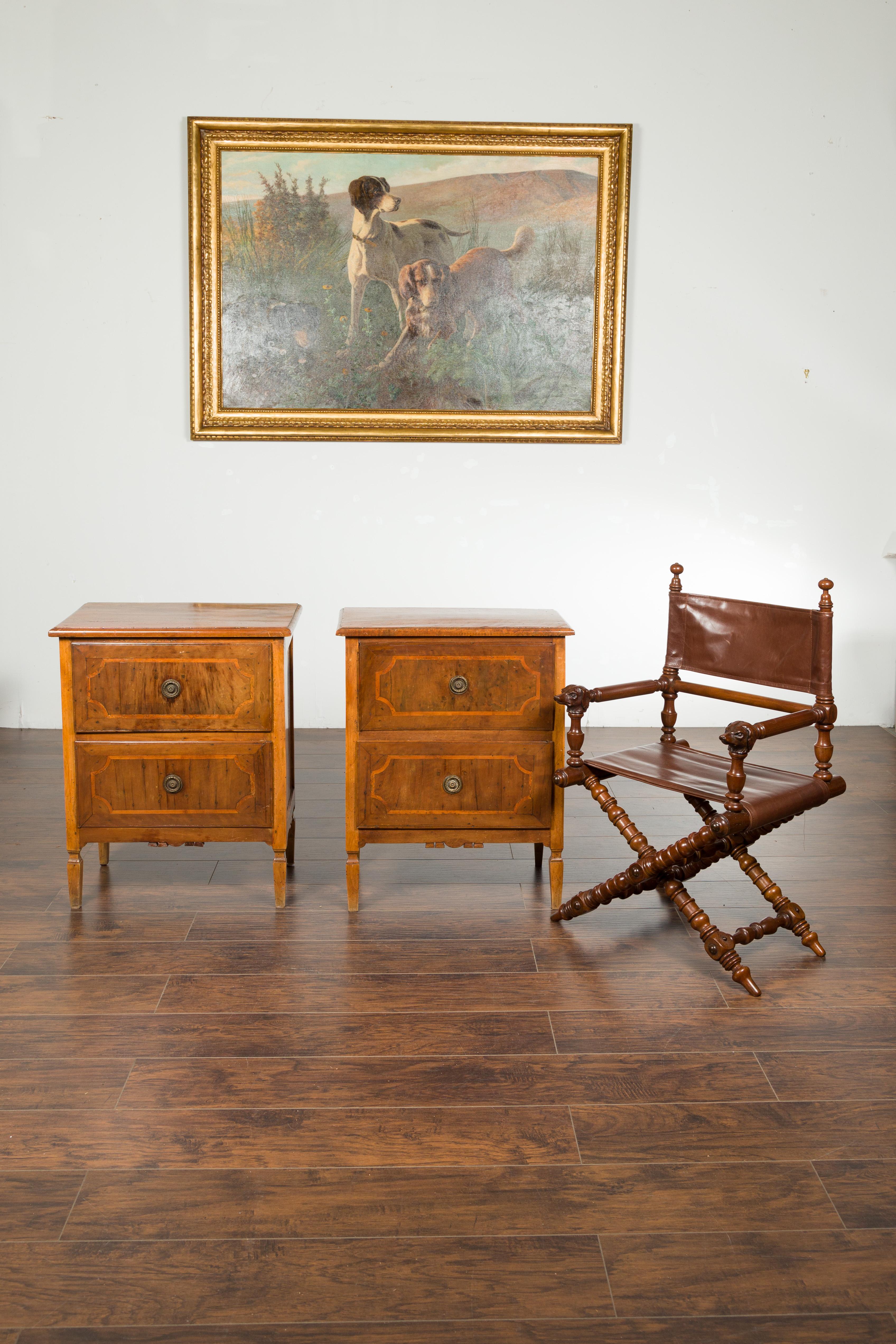 A pair of petite Italian walnut two-drawer chests with banding, carved aprons and tapered feet. Created in Italy during the first quarter of the 19th century, each of this pair of chests features a rectangular top sitting above two drawers, adorned