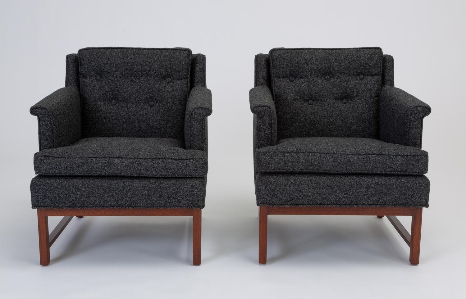 A pair of lounge chairs, upholstered in a heather midnight blue fabric, designed by Edward Wormley for Dunbar. The fully restored pair have a cubic design, with a slightly angled backrest and key arms. The body of the chair sits on a walnut-stained