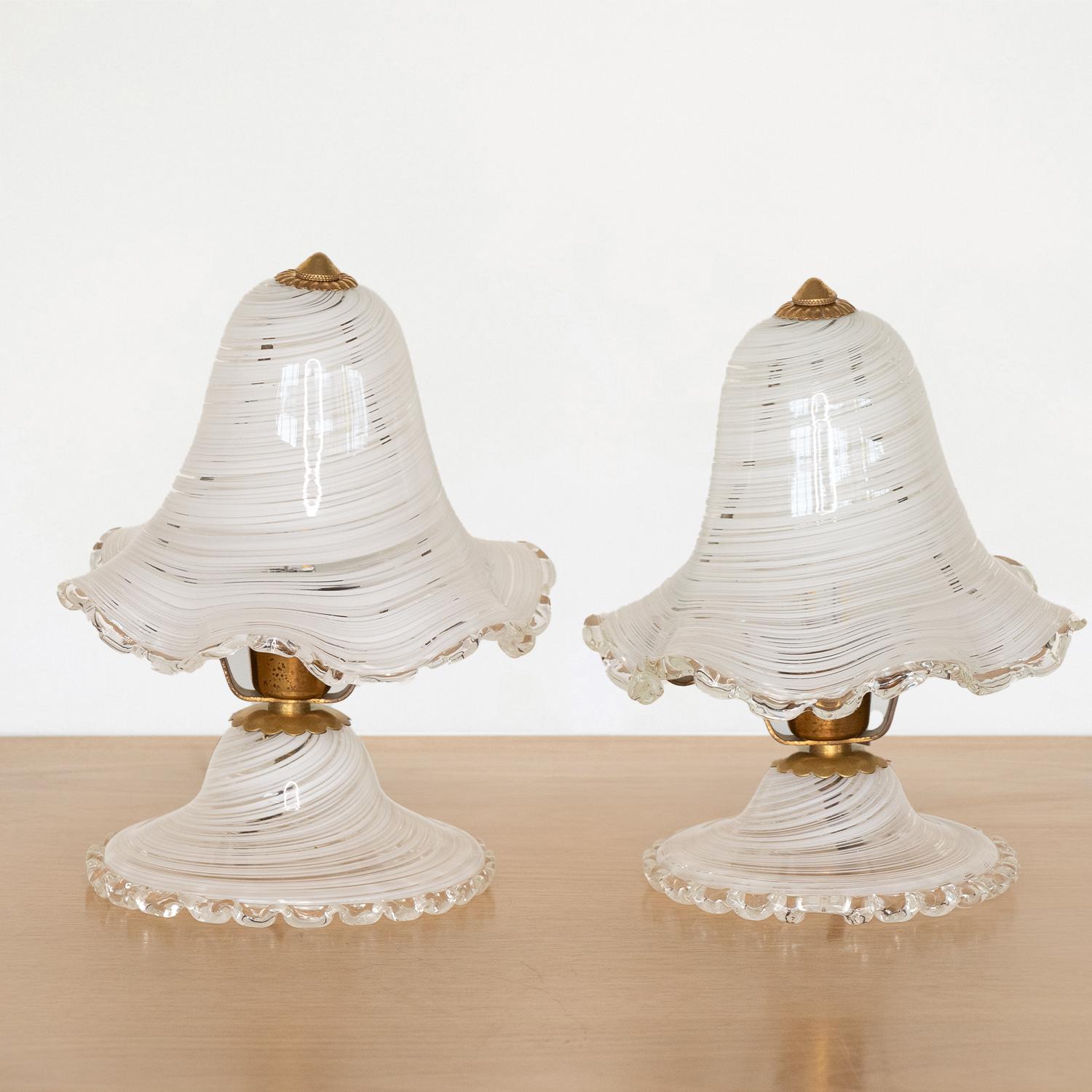 Stunning pair of petite Murano glass lamps from Italy, 1940s. Beautiful swirled white glass bell shade with scalloped rim, scalloped glass base and brass detailing. Newly rewired with brown cloth twist cord. Beautiful age and patina to the brass.