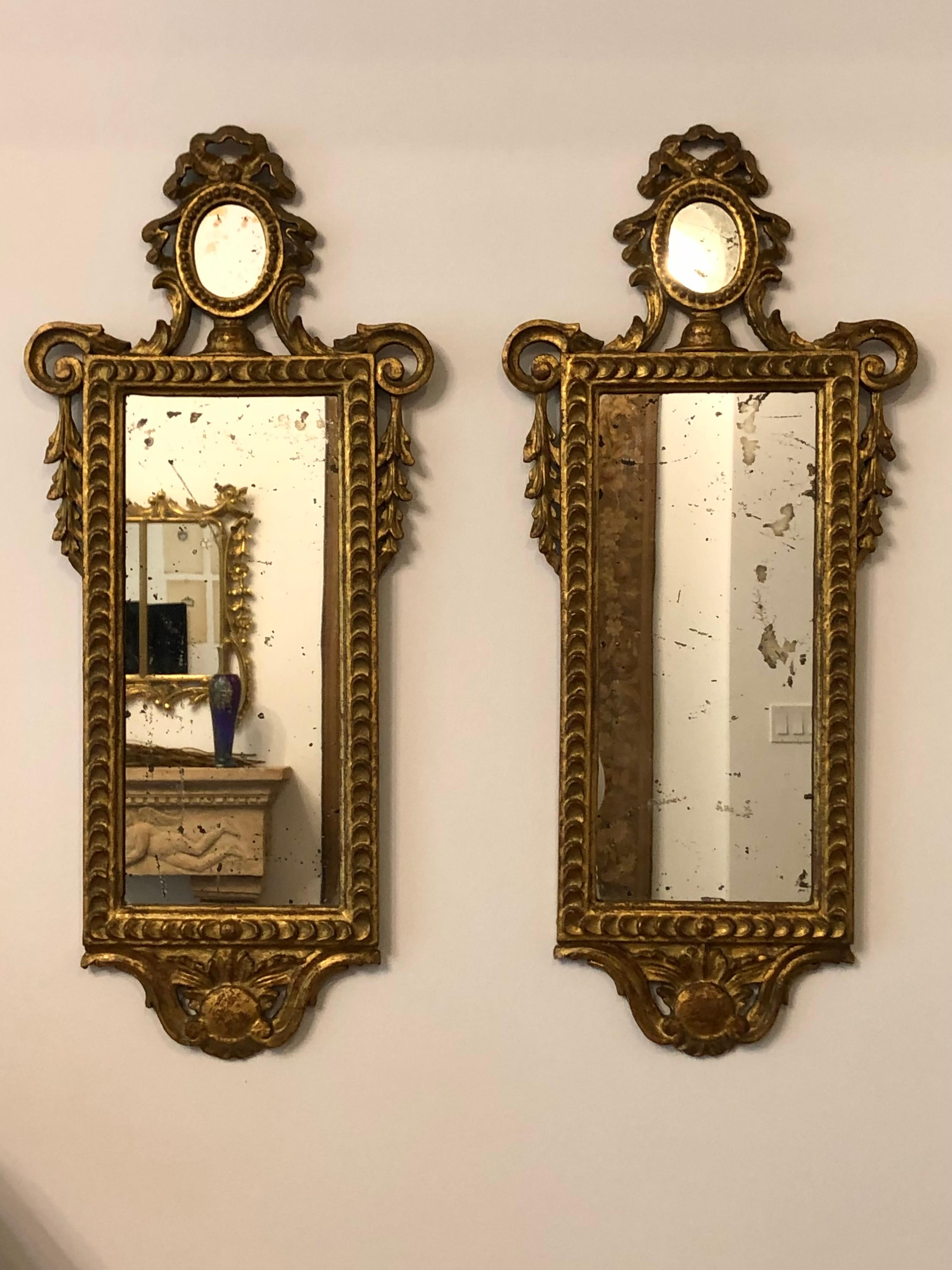 This is a lovely pair of petite Neoclassical mirrors. Rectangular mirrors surmounted by oval rosettes with ribbons, swags and beading. Beautiful oxidation to the glass. Most probably French.
These mirrors are in good condition with some instability