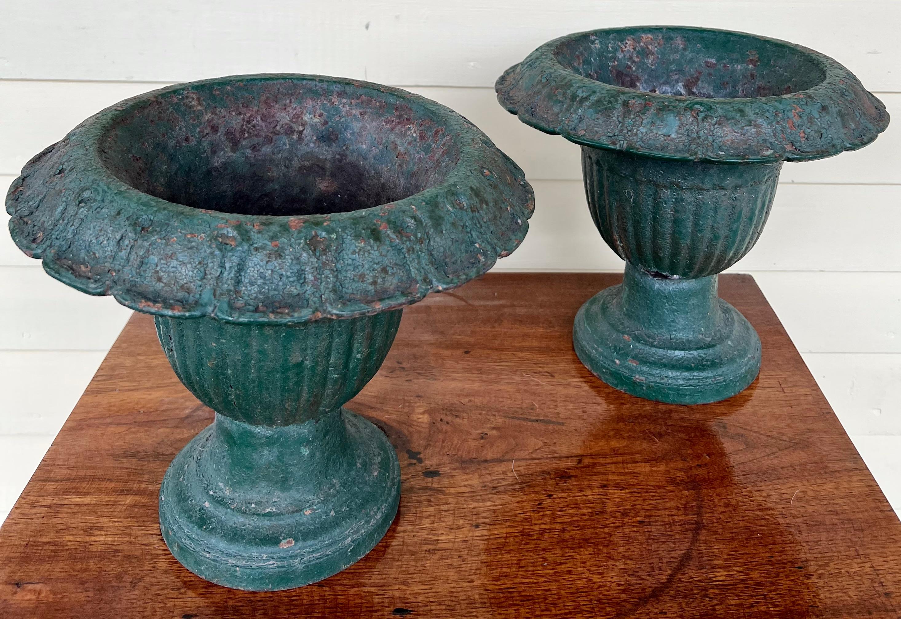 Unusal small sized pair of green painted cast iron urns. The paint is early and the patina is beautifully worn. There is one chip out of one of the bases, but it may have been a dent or done in production as the area has the same early green paint