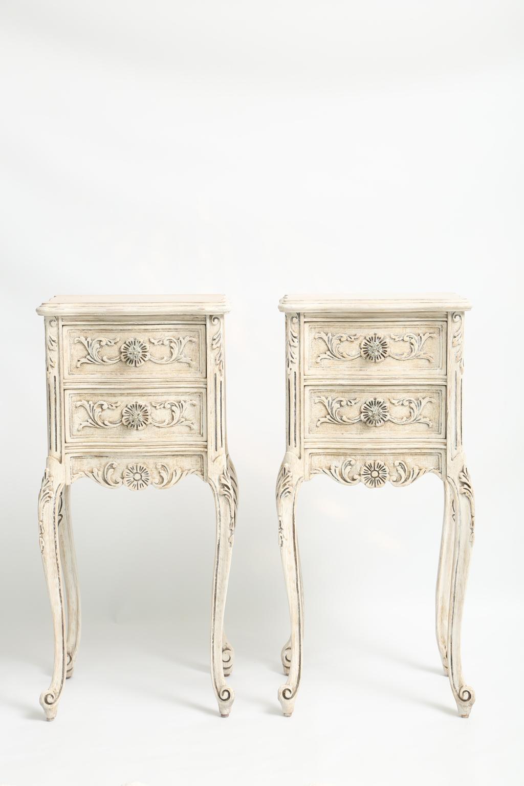 Pair of nightstands, having a painted finish, each molded top over two stacked drawers, their flowerhead-pulls flanked by foliate carving, stiles carved with acanthus and fluting, over shaped apron centered by a rosette, raised on cabriole legs,