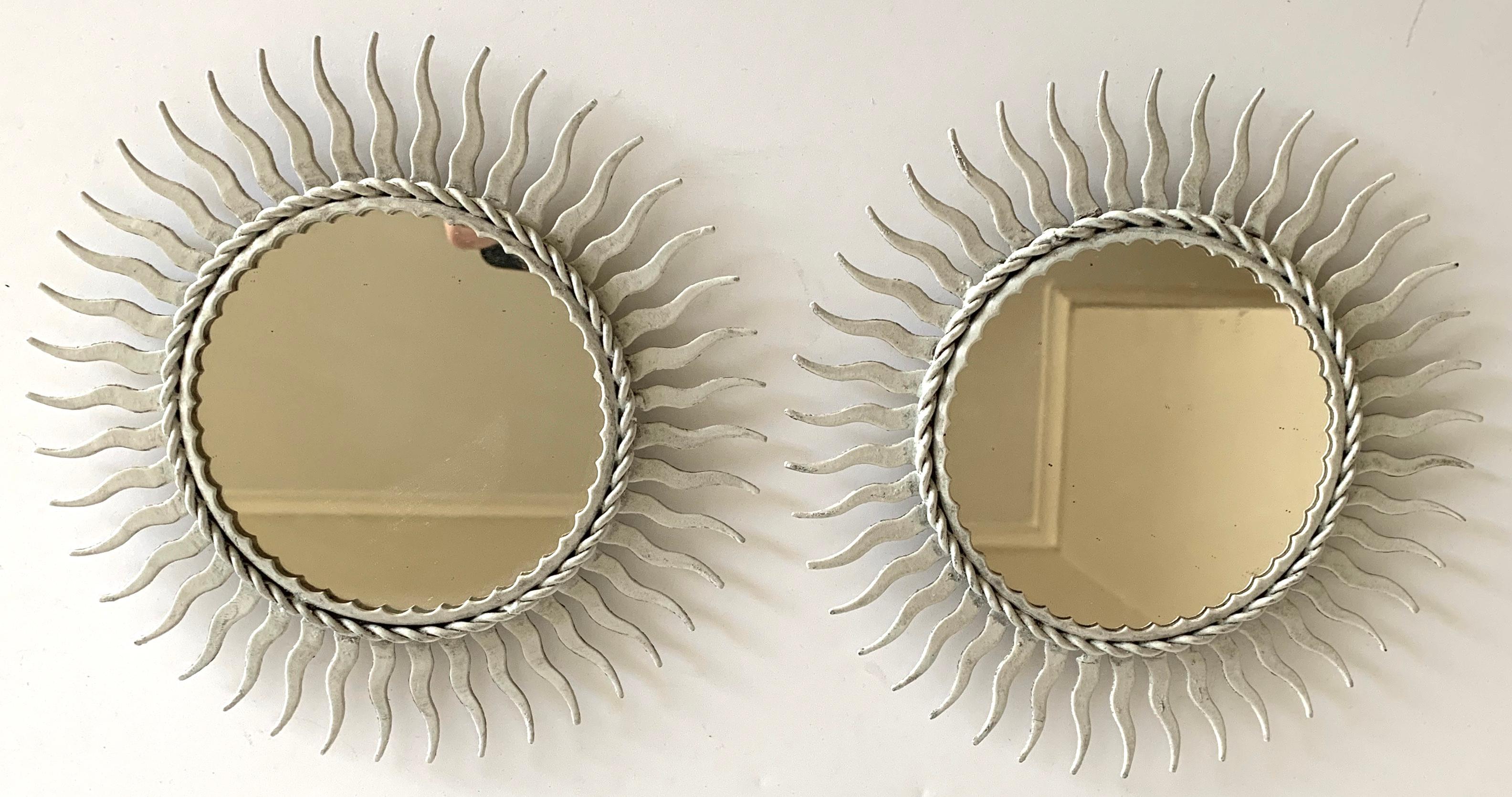 Pair of petite painted metal sunburst mirror. Newly painted in an antique white finish with original mirrored glass. Hanging hardware not included.