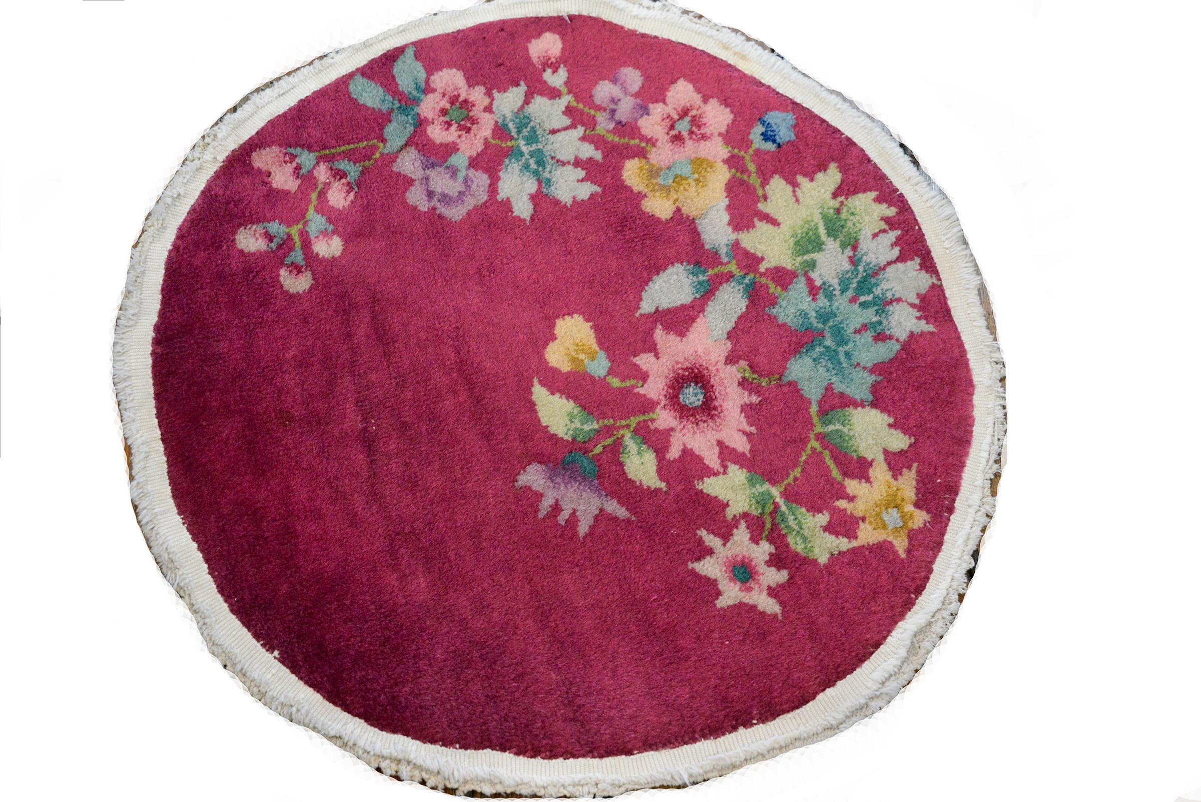A pair of petite early 20th century Chinese Art Deco rugs each with multicolored peonies and chrysanthemums against a rich fuchsia background.