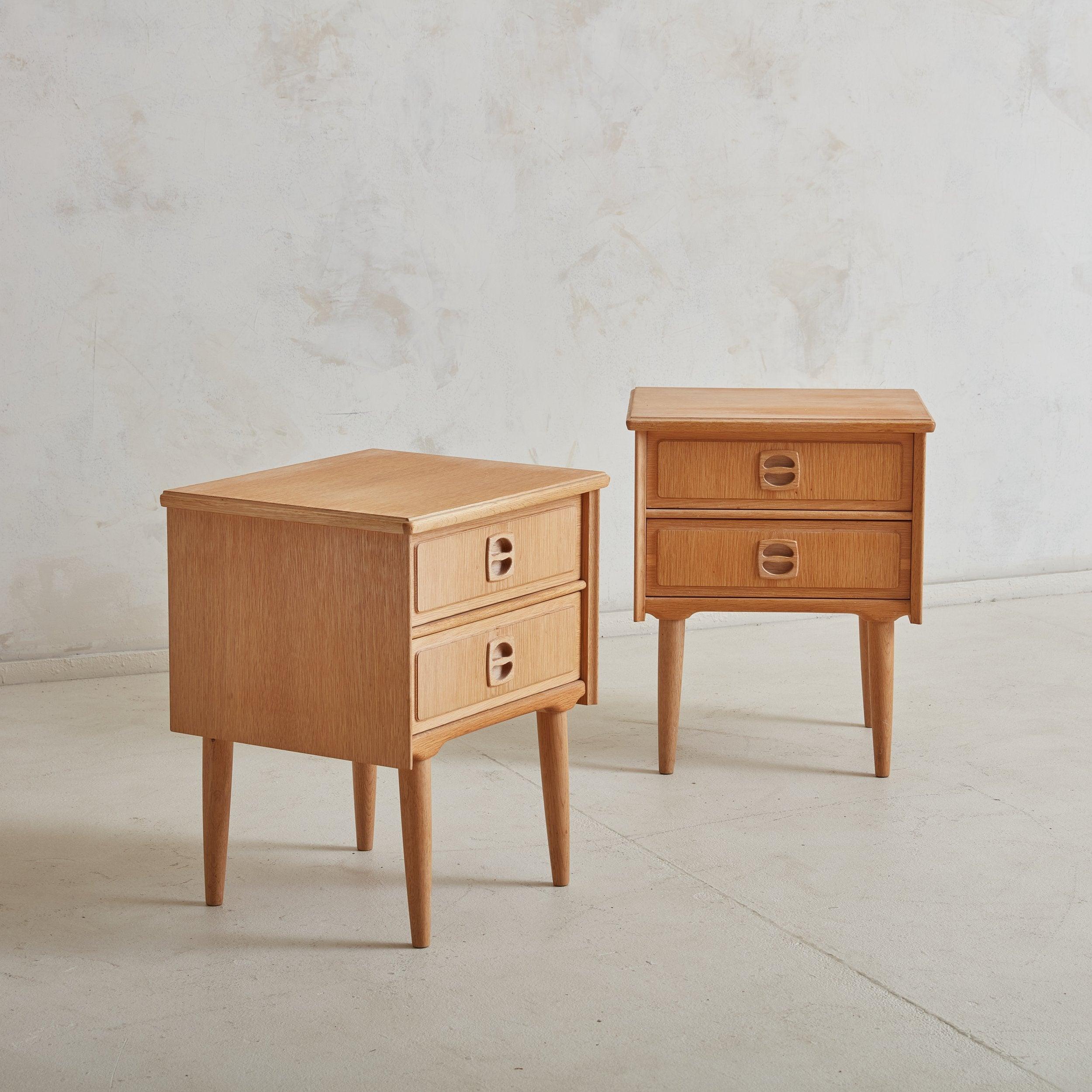A pair of Scandinavian Modern rectangular nightstands composed of beautifully grained solid oak in a light finish. These petite nightstands feature tapered legs and double drawers with layered surface details and circular inset handles. Denmark,