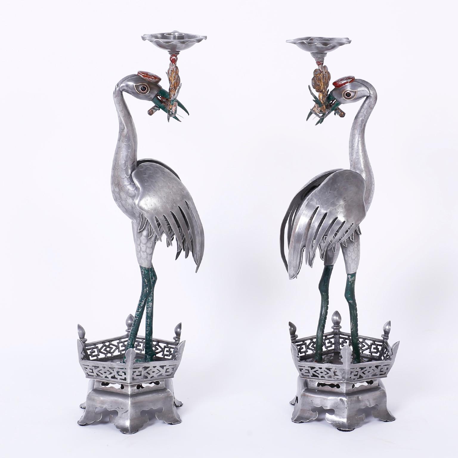 Pair of antique Chinese pewter bird candlesticks portraying storks or cranes holding floral candle cups in their beaks, retaining their original time-worn decorative paint and featuring engraved details and classic Ming style bases.
 