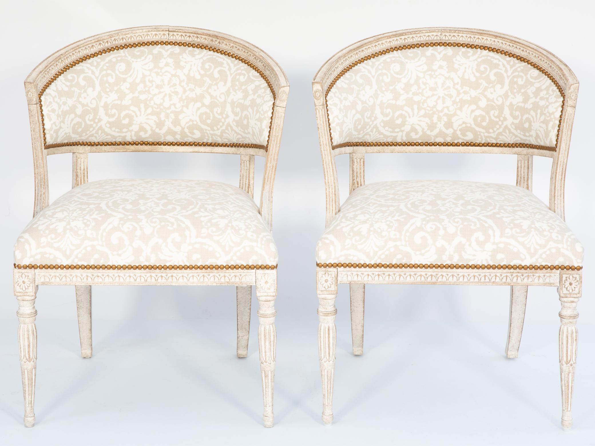 Paire de fauteuils baquets de style gustavien avec finition peinte montrant une usure naturelle, chaque dossier arqué et courbé, cannelé, sculpté de godrons et tapissé de lin imprimé Rococo avec des têtes de clous, reposant sur des montants cannelés