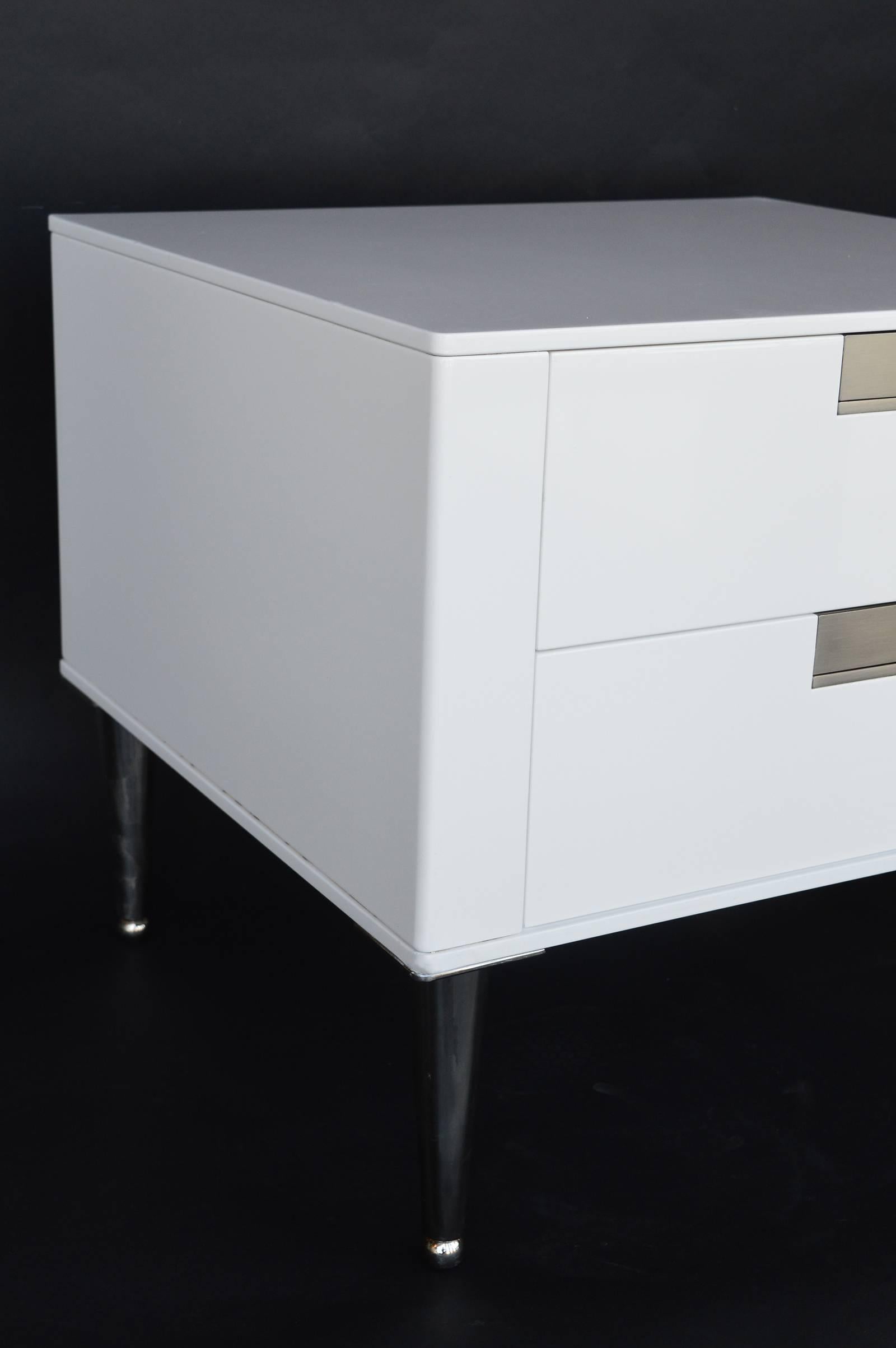 White two drawered nightstands with sleek handles. Sticker is on the top outer edge of the drawer.