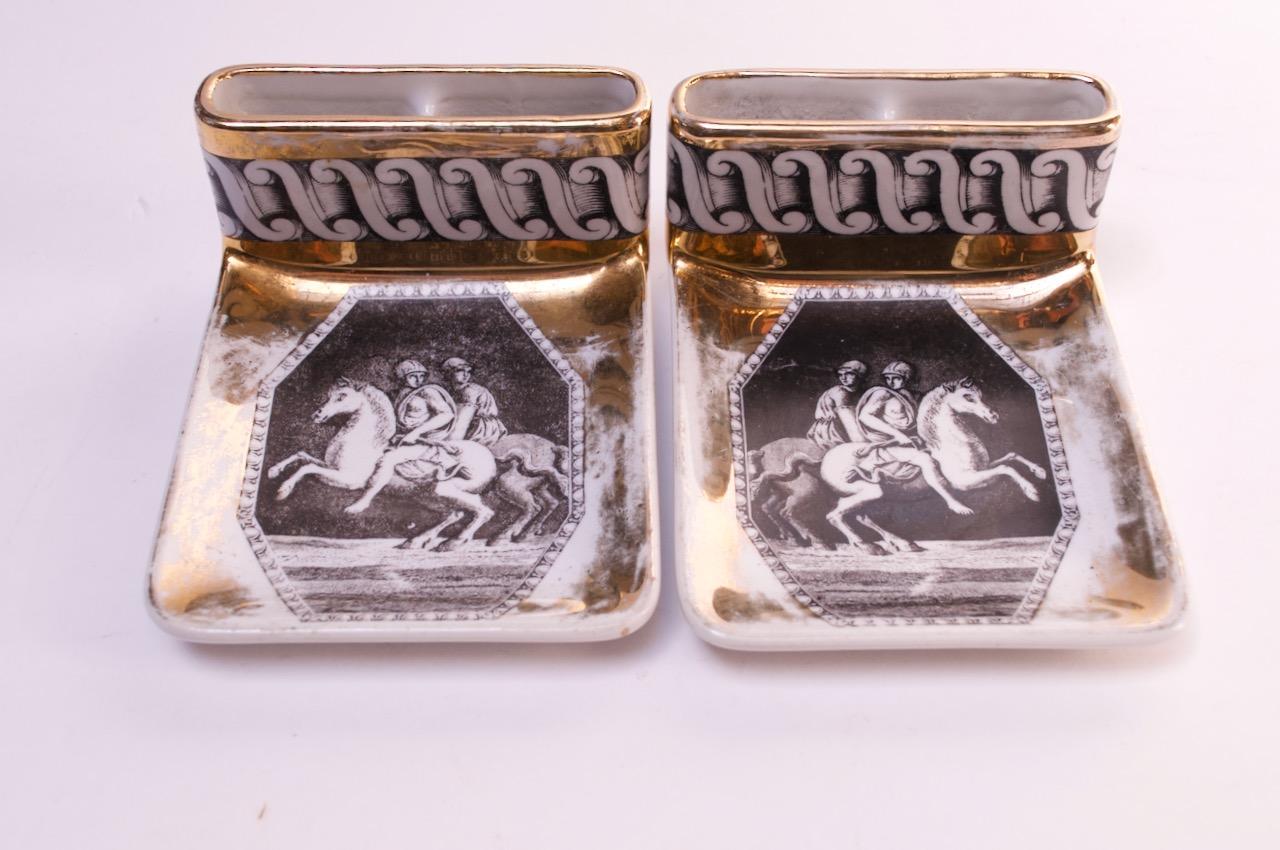 Pair of ashtrays with cigarette slots by Piero Fornasetti, (circa 1950s, Italy). These examples retailed at Bergdorf Goodman in New York City, as indicated on the reverse. Composed of a grey printed equestrian motif with scroll border and gilded