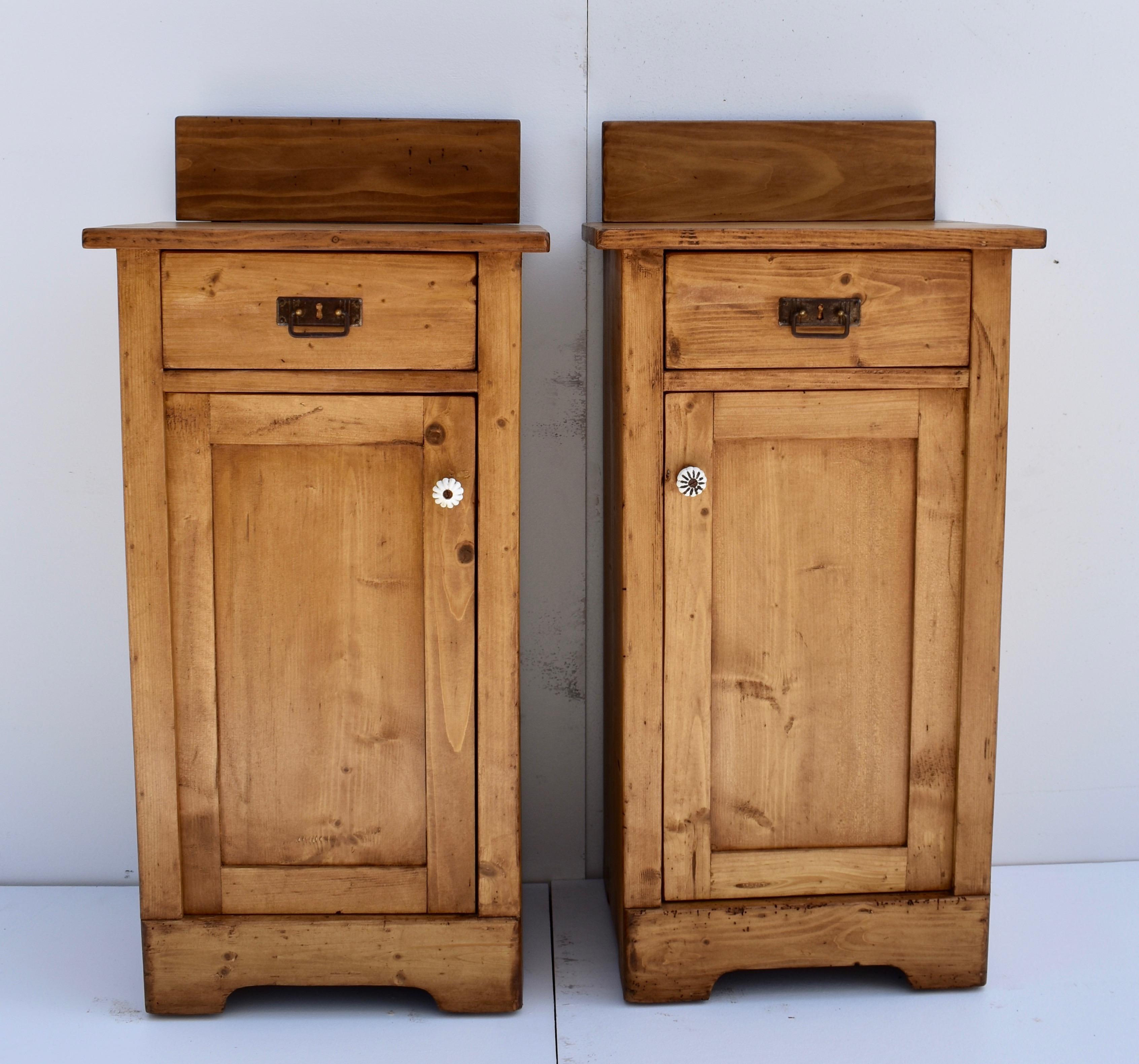 This pair of polished pine nightstands is in the usual one door, one-drawer configuration. The straight-topped removable splashback is finished in a contrasting rugger brown wax. The drawer is of handcut dovetailed construction and the paneled door