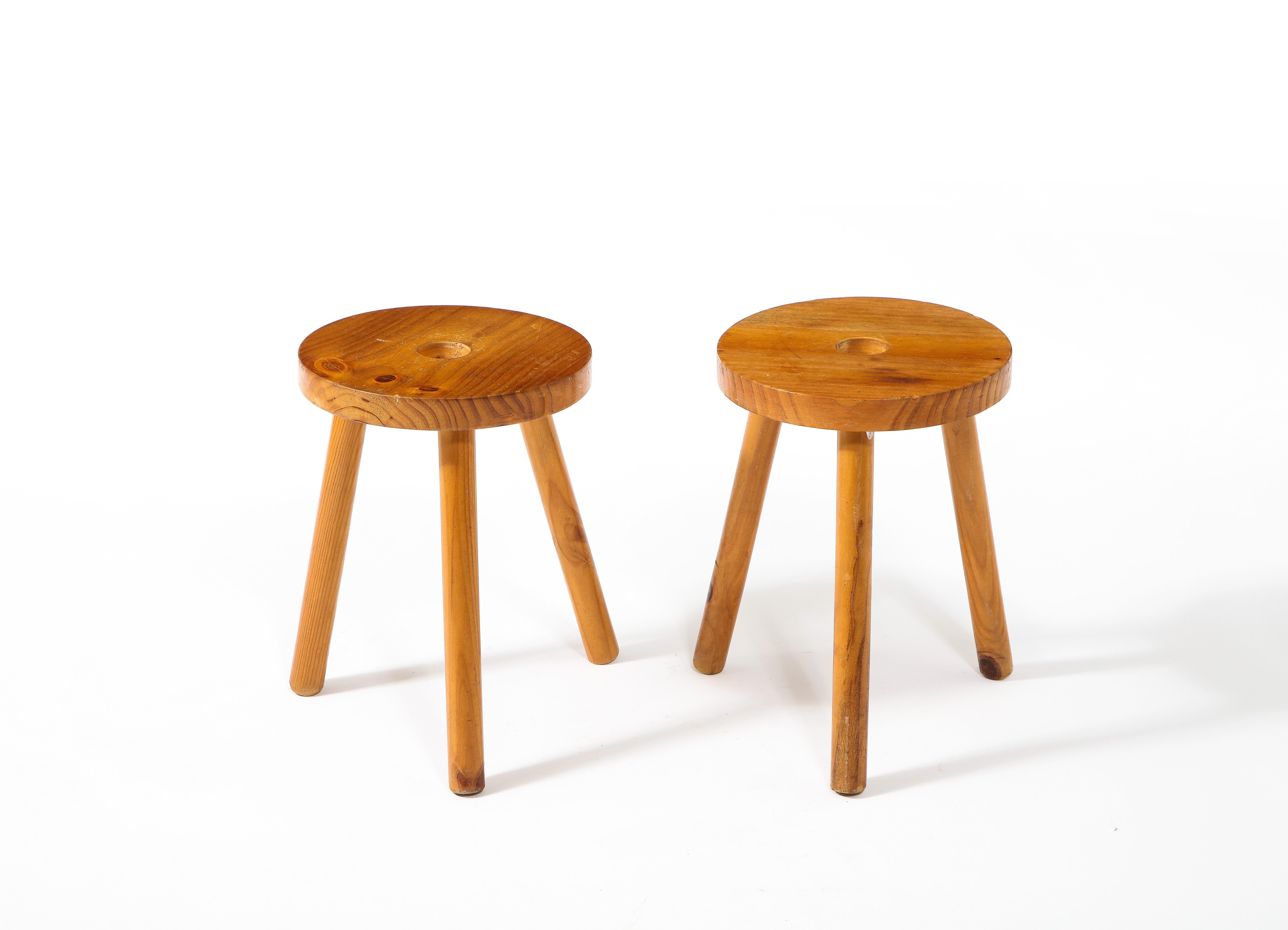 A pair of pine tripod stools with a center hole in the seat. They unscrew entirely for shipping.