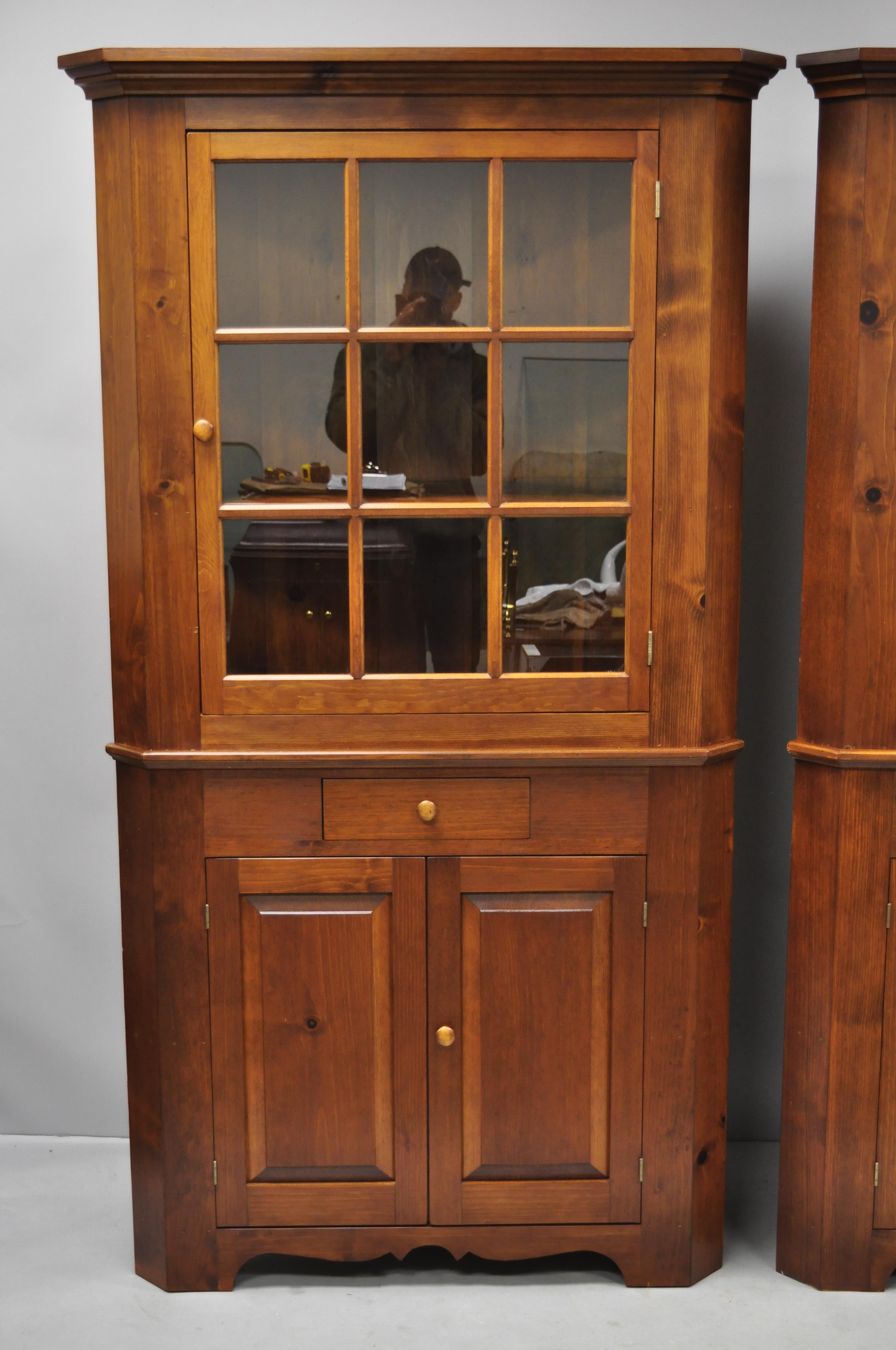 Pair of pine wood Colonial style corner cupboard China cabinets by Tom Seely. Items feature solid wood construction, beautiful wood grain, 2 part construction, glass swing doors, plate groves, 1 dovetailed drawers, quality American craftsmanship,