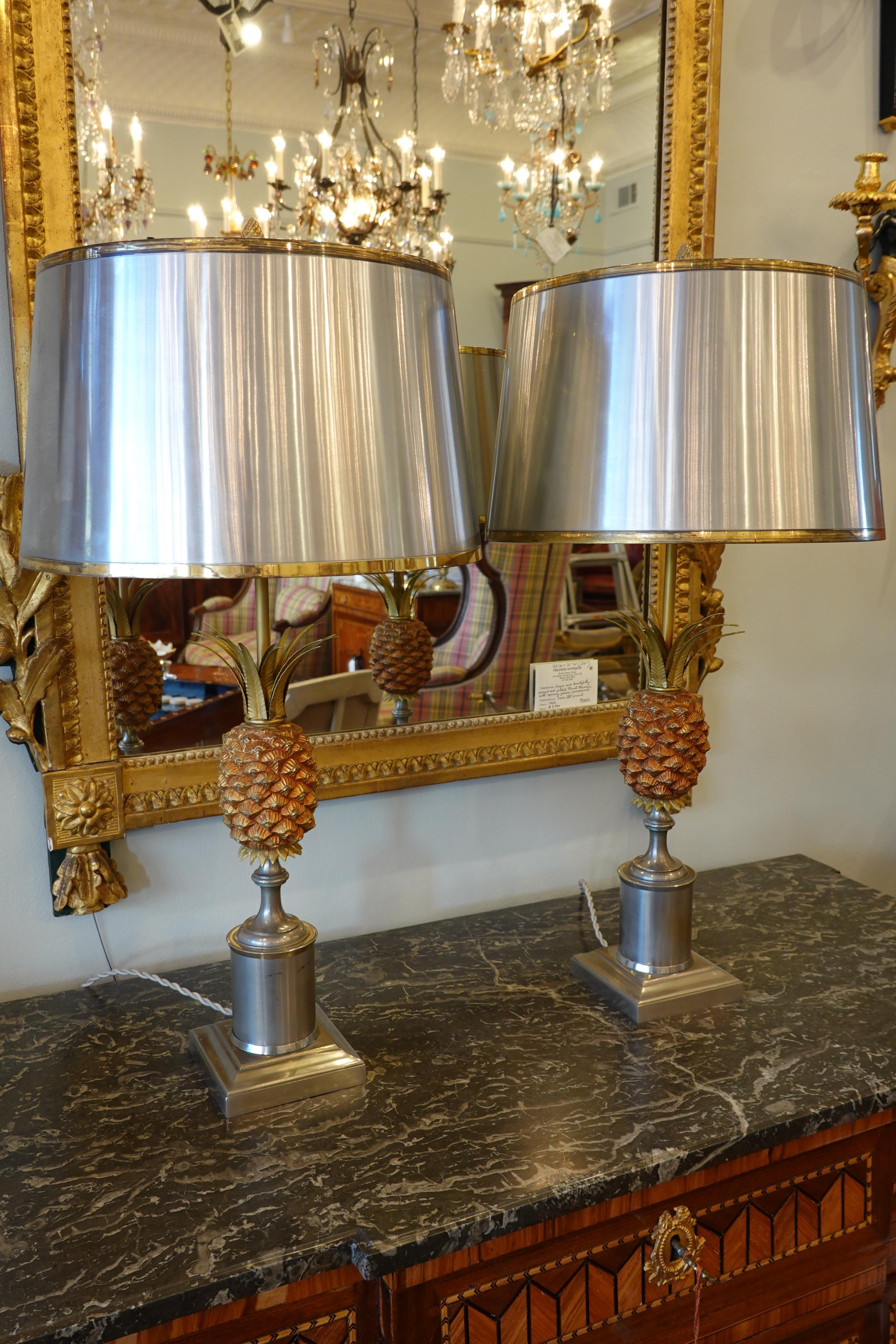 Pair of brushed steel lamps featuring a pineapple and steel shade in the style of Maison Jansen or Maison Charles. The shade is brushed steel to match the lamp base with brass trim, and has a stylized pine cone finial. The lamps have been rewired