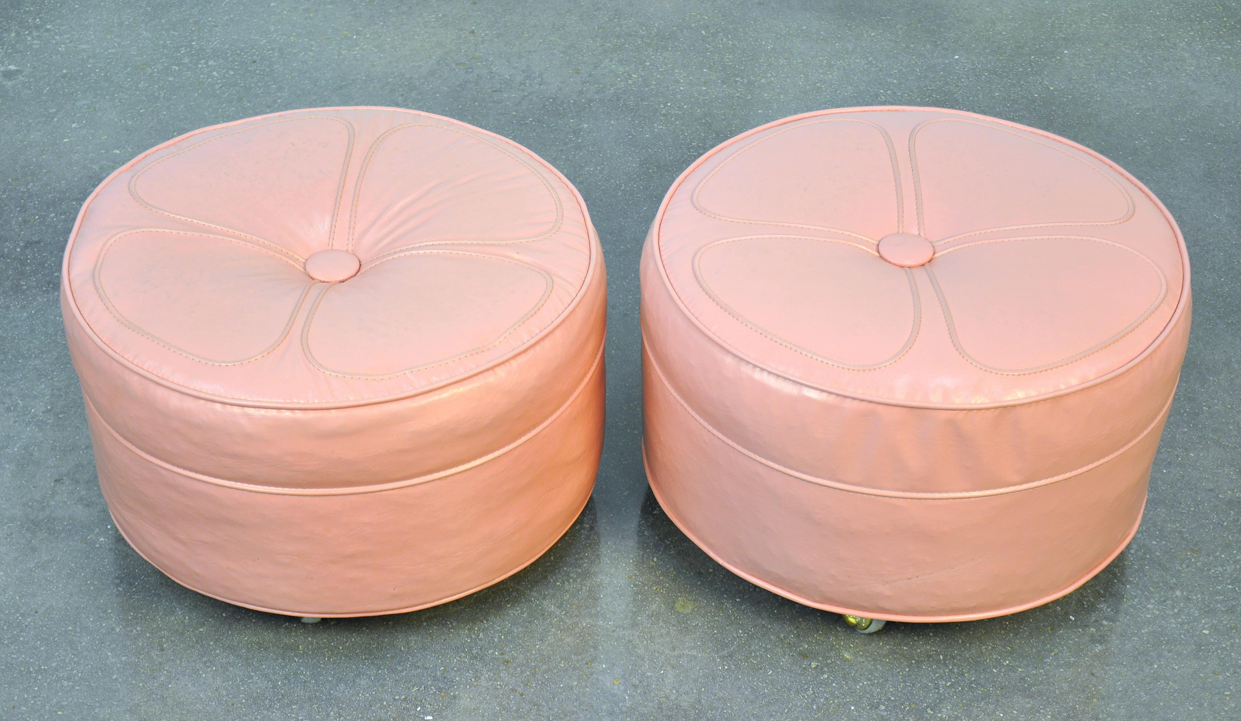 A vintage set of Mid-Century Modern rolling poufs featuring their original soft pastel pink upholstery and brass casters. The footstools have a nice Hollywood Regency flair to them.