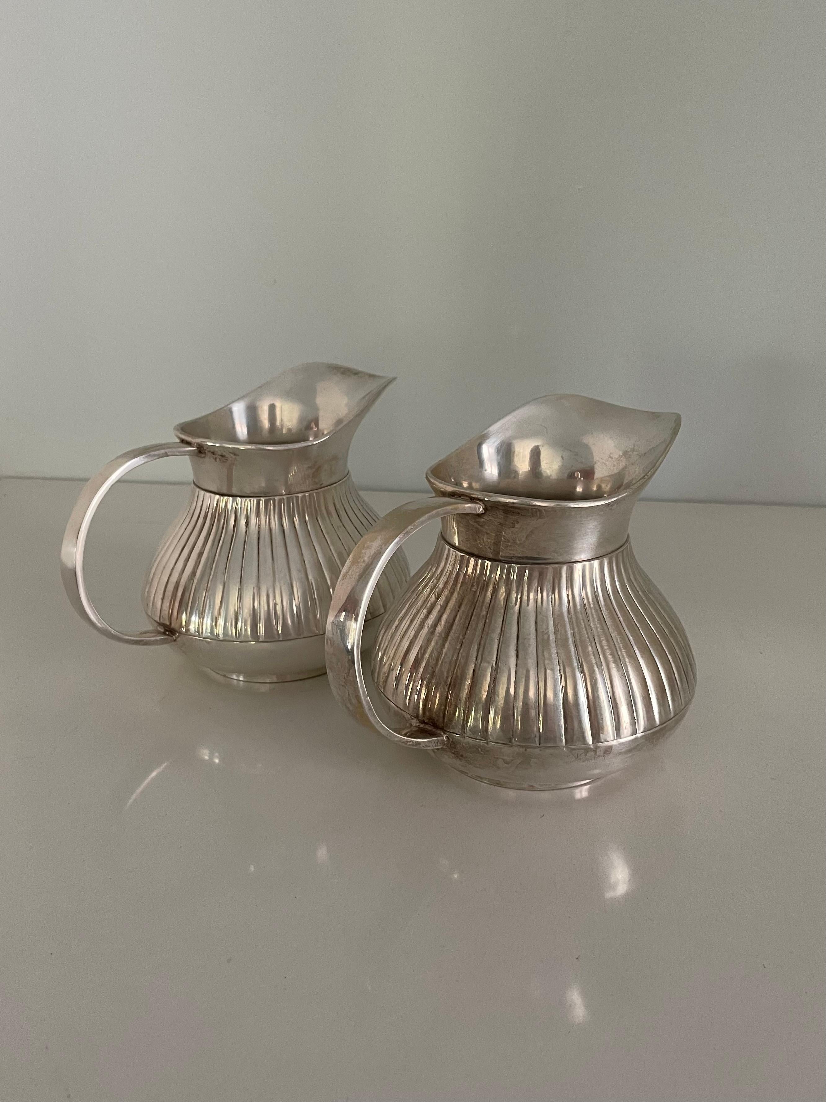 Pair of shining silver pitchers perfect for tea time. Wonderful pinstriping on the body and a solid handle. Similar to Georg Jensen Scandinavian Design. These pitchers are ideal to hold various alternative milks at brunch.