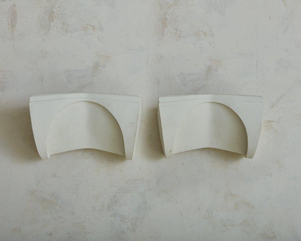 A pair of 1980s sculptural plaster sconces by Boyd Lighting Company. These sconces feature a rectangular shape with elegant curves and angled cutouts to emanate warm light. They have a raised ‘Copyright Boyd 9676’ mark + retain ‘Boyd Lighting