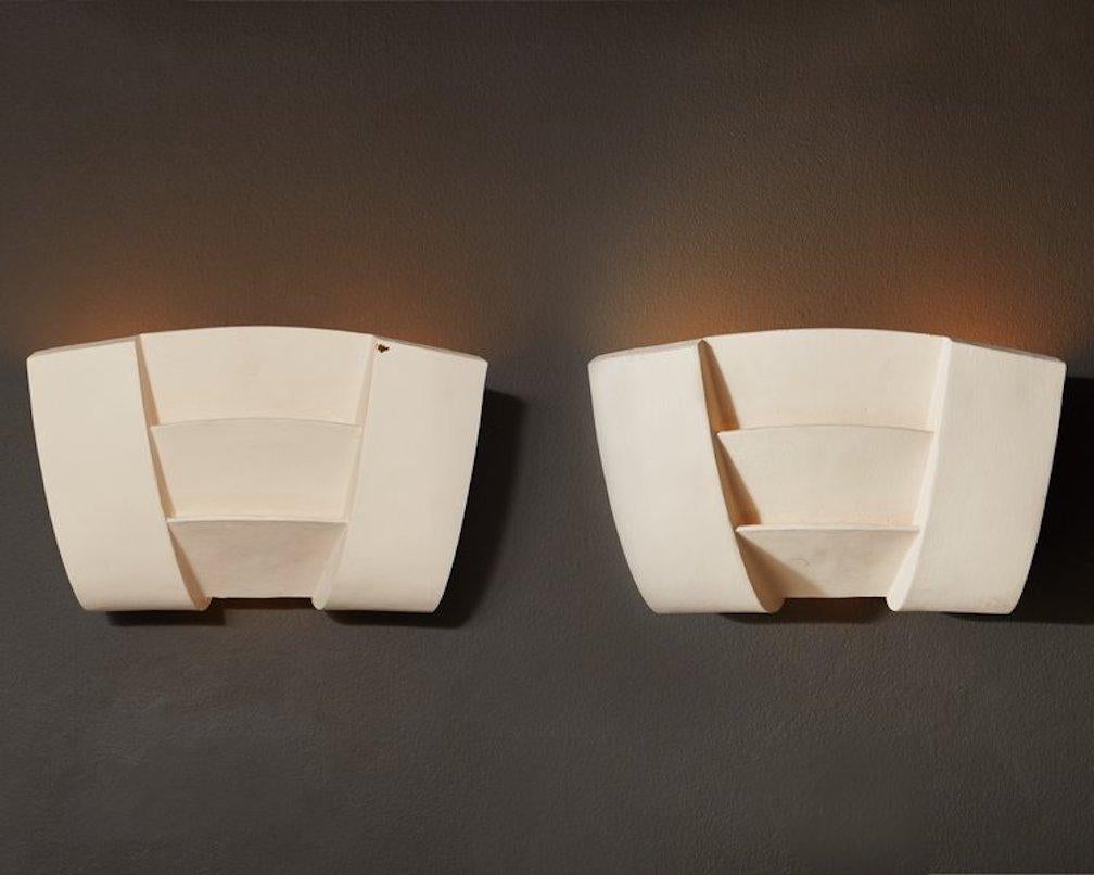 A pair of sculptural plaster sconces designed by Charles Pfister for Boyd in 1987. These sconces feature a rectangular shape with elegant curves and angled cutouts to emanate warm light. Signed on inside and has a raised ‘Copyright Boyd 9632’ mark.