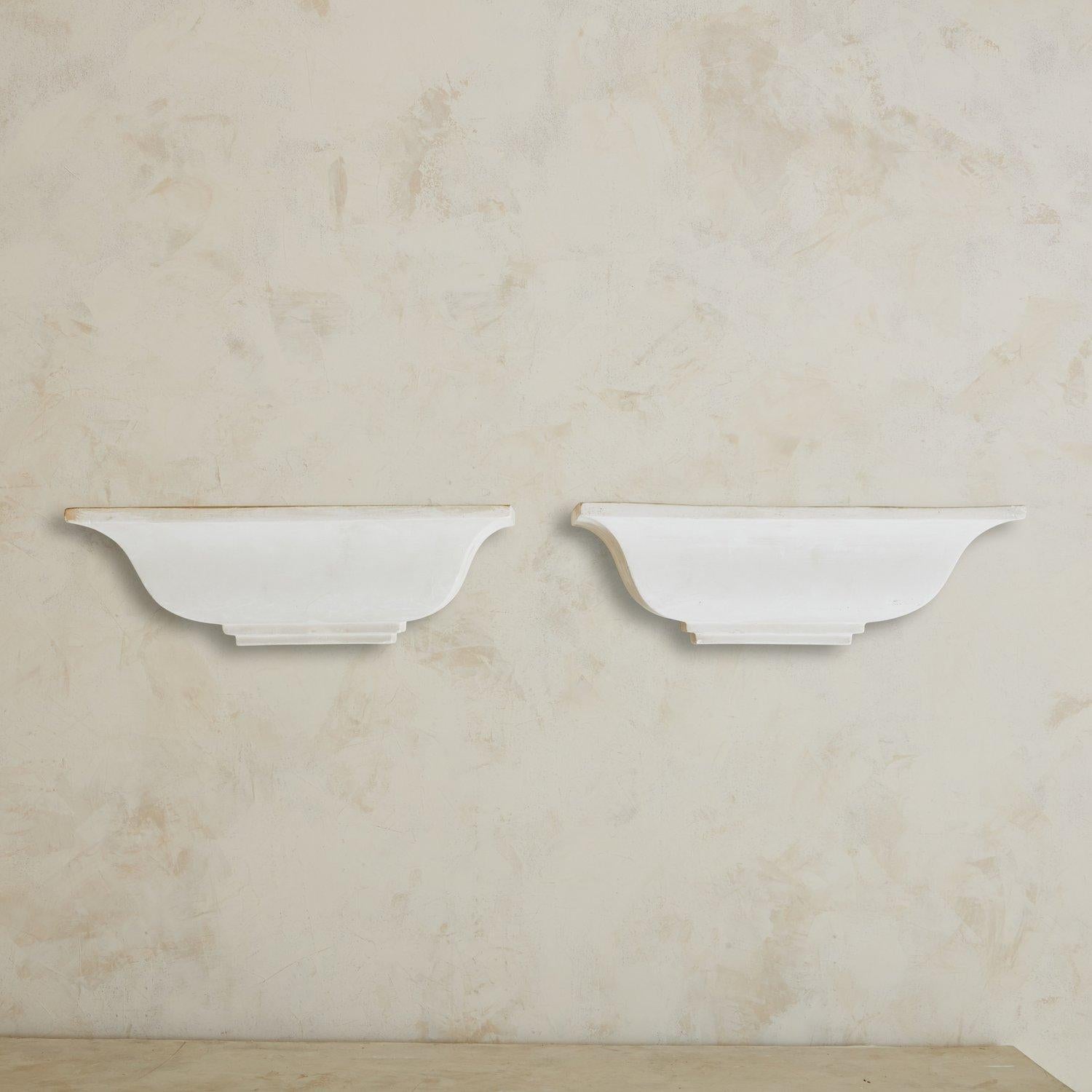 A pair of French wall sconces featuring an elegant plaster tiered base that supports a tapered, rectangular plaster shade. The subdued white tone of these fixtures would stand out in any space and their classic shape holds a timeless appeal. 1930s.