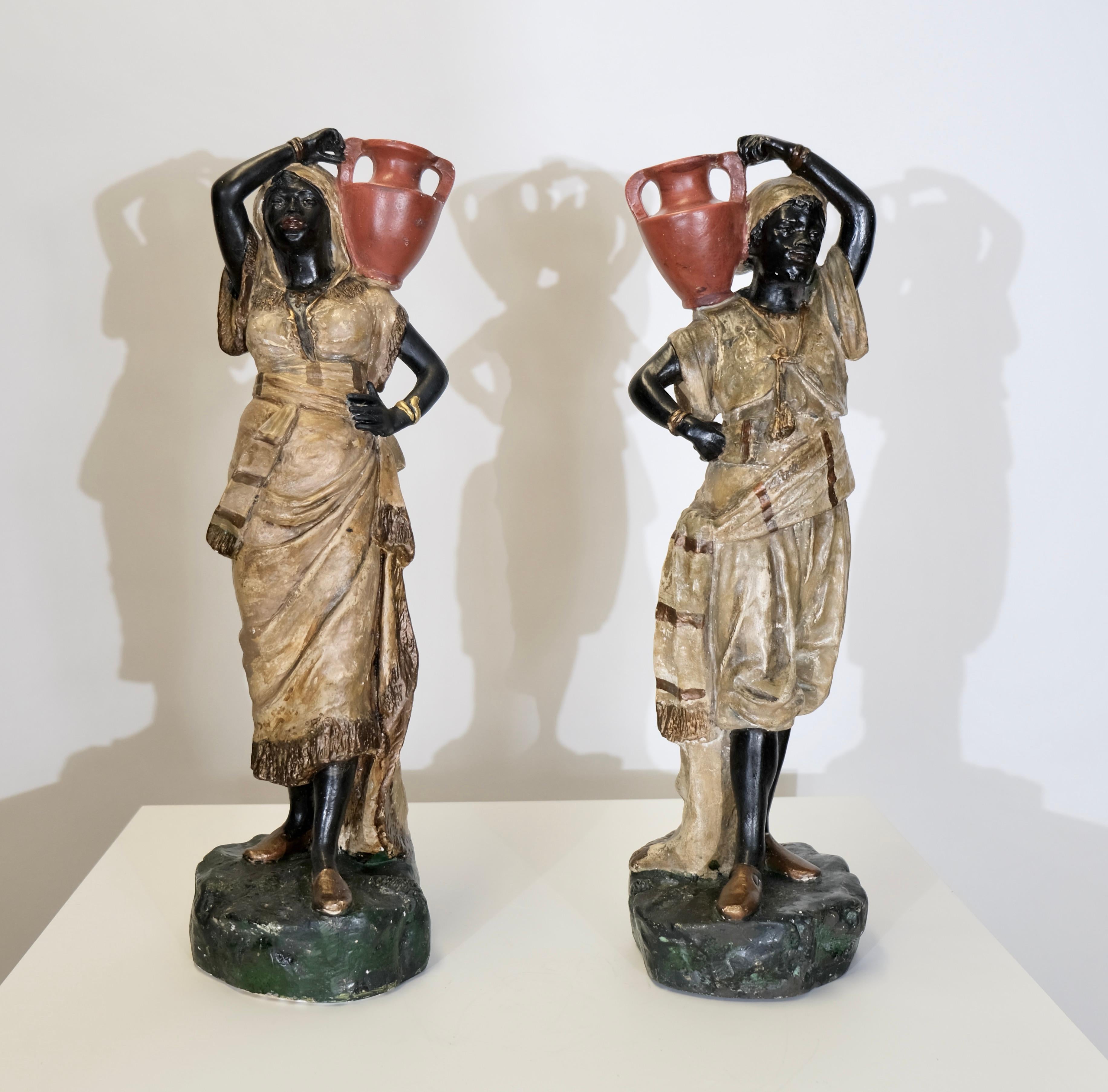 Este par de esculturas austriacas de yeso, creadas hacia 1900, representan a dos mujeres elegantemente vestidas que llevan ánforas al hombro. Sus detallados ropajes, posturas expresivas y rasgos finamente pintados reflejan el estilo artístico de