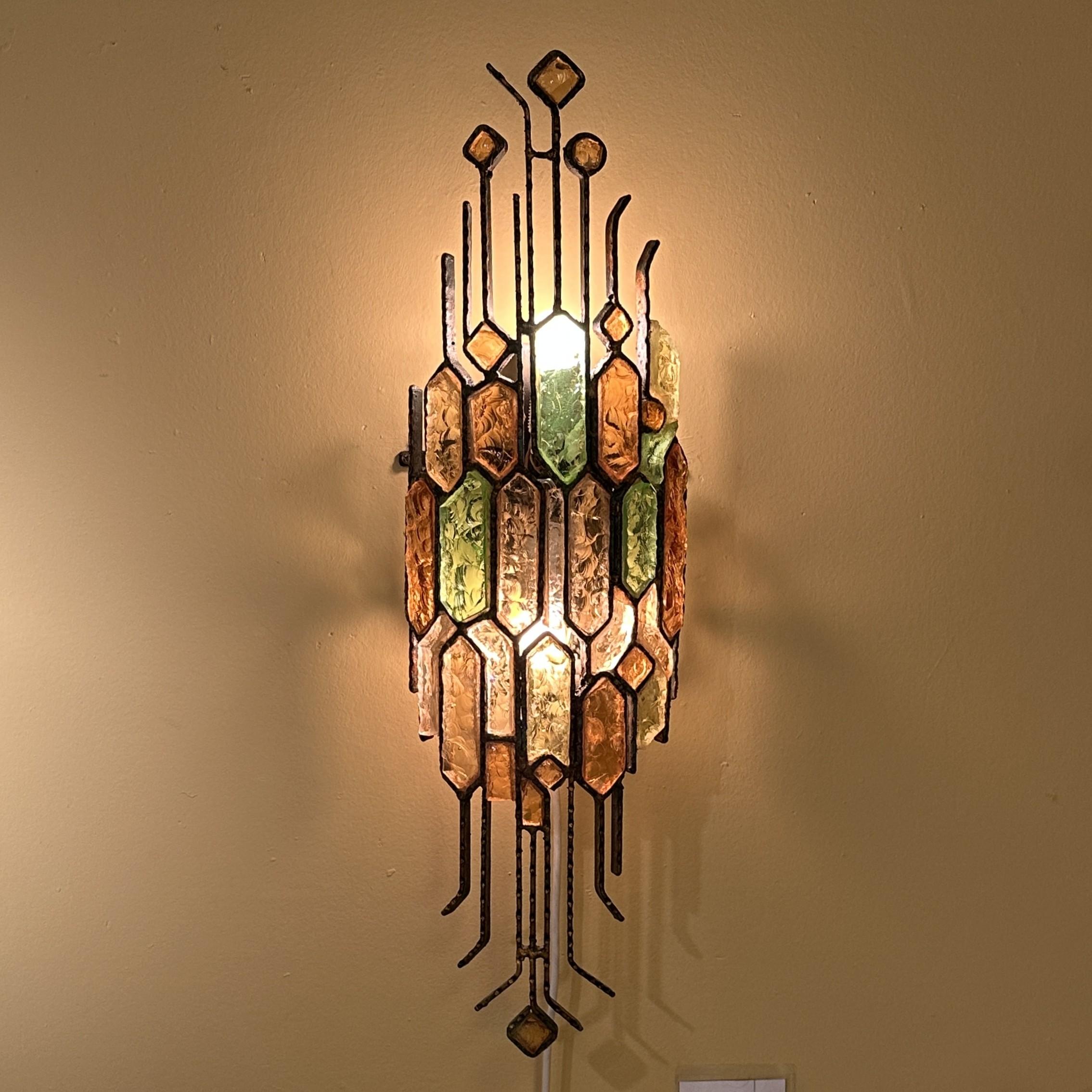 Pair of brutalist Poliarte Wall Sconces, by Albano Poli, Italy 1960's hand forged hammered steel holding thick multi coloured faceted Murano glass, 1970's. 
Chiselled hammered pieces of glass are set in a frame of wrought iron holders, following the