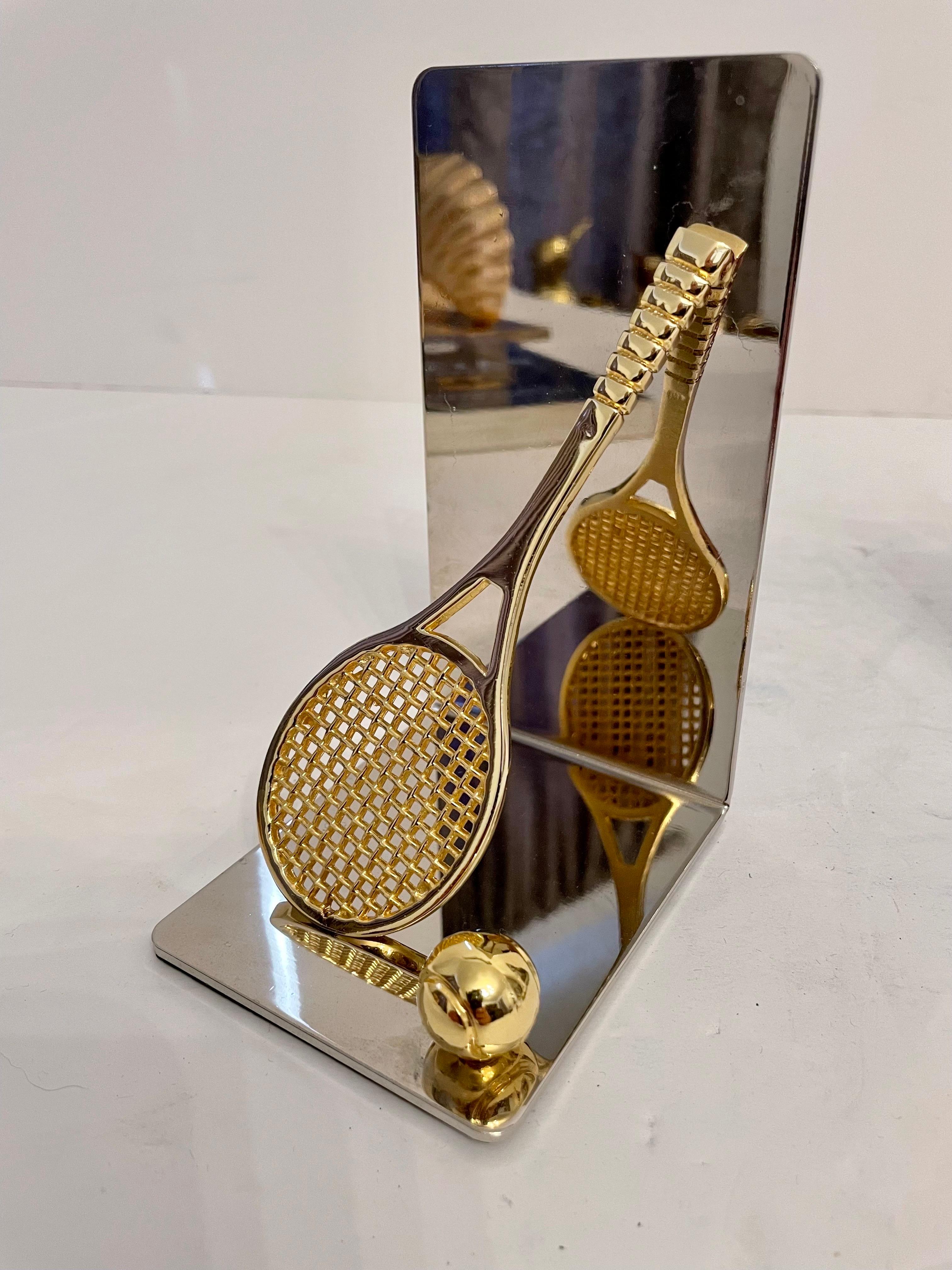 Set of brass and chrome tennis racket bookends. Features a brass tennis racket and ball on each. Has thin foam on bottom of each to prevent scratching furniture. 5.5
