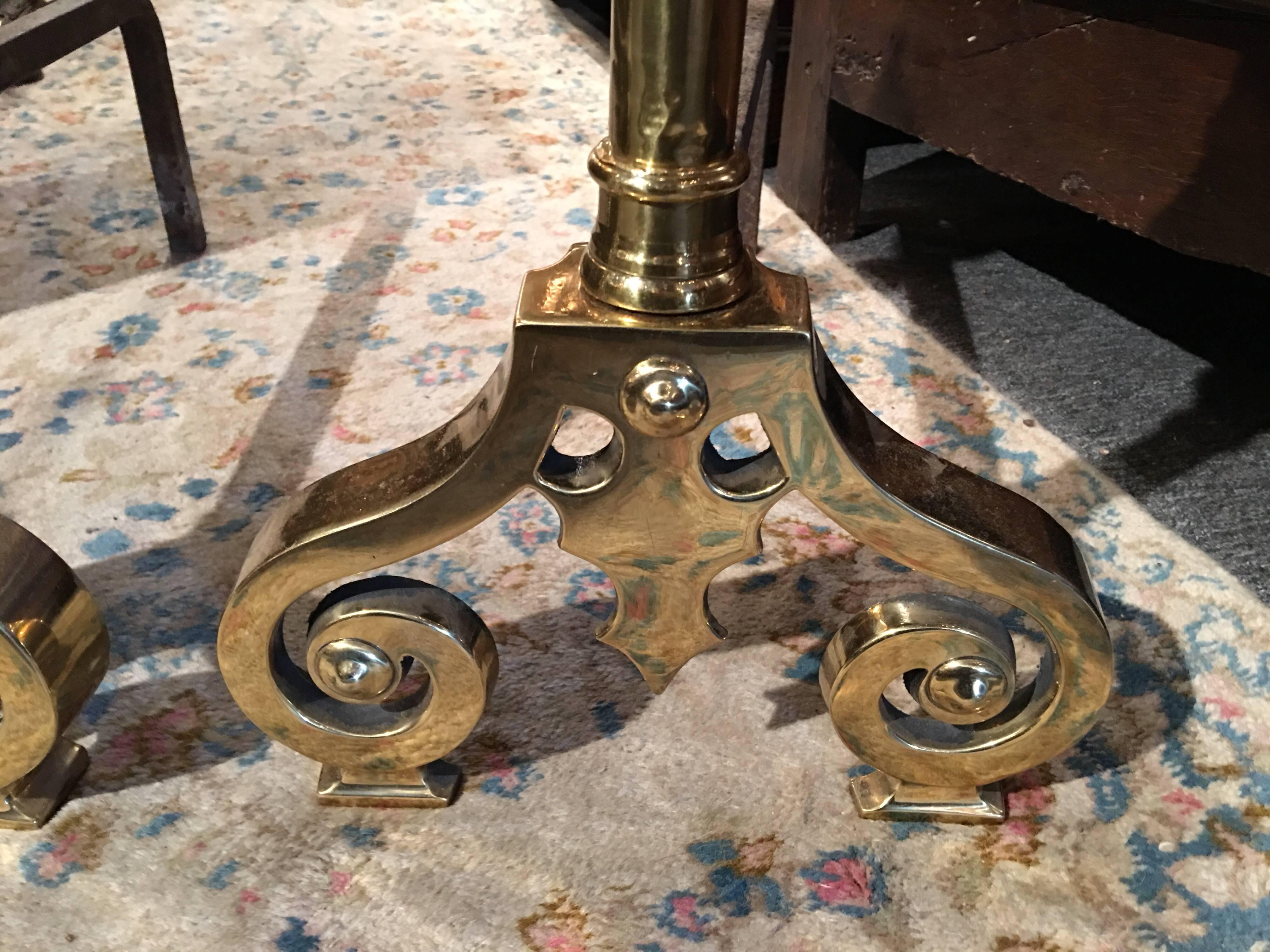 Pair of polished brass chenets or andirons with decorative scrolls and towering finials, 19th century.
