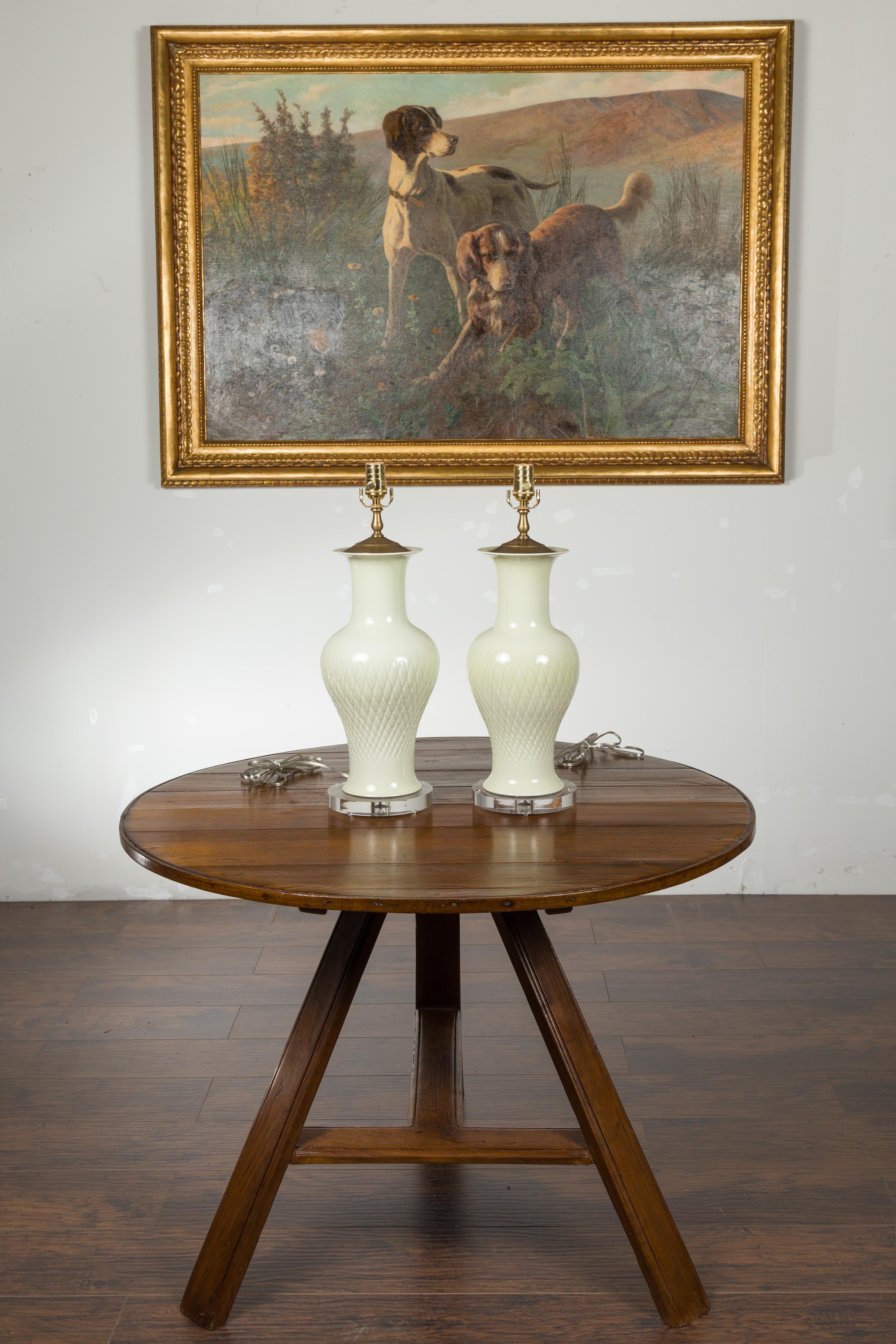 A pair of porcelain white table lamps from the late 20th century, with round lucite bases. Created during the second half of the 20th century, each of this pair of porcelain lamps features elegant vase-shaped silhouettes adorned with crosshatched