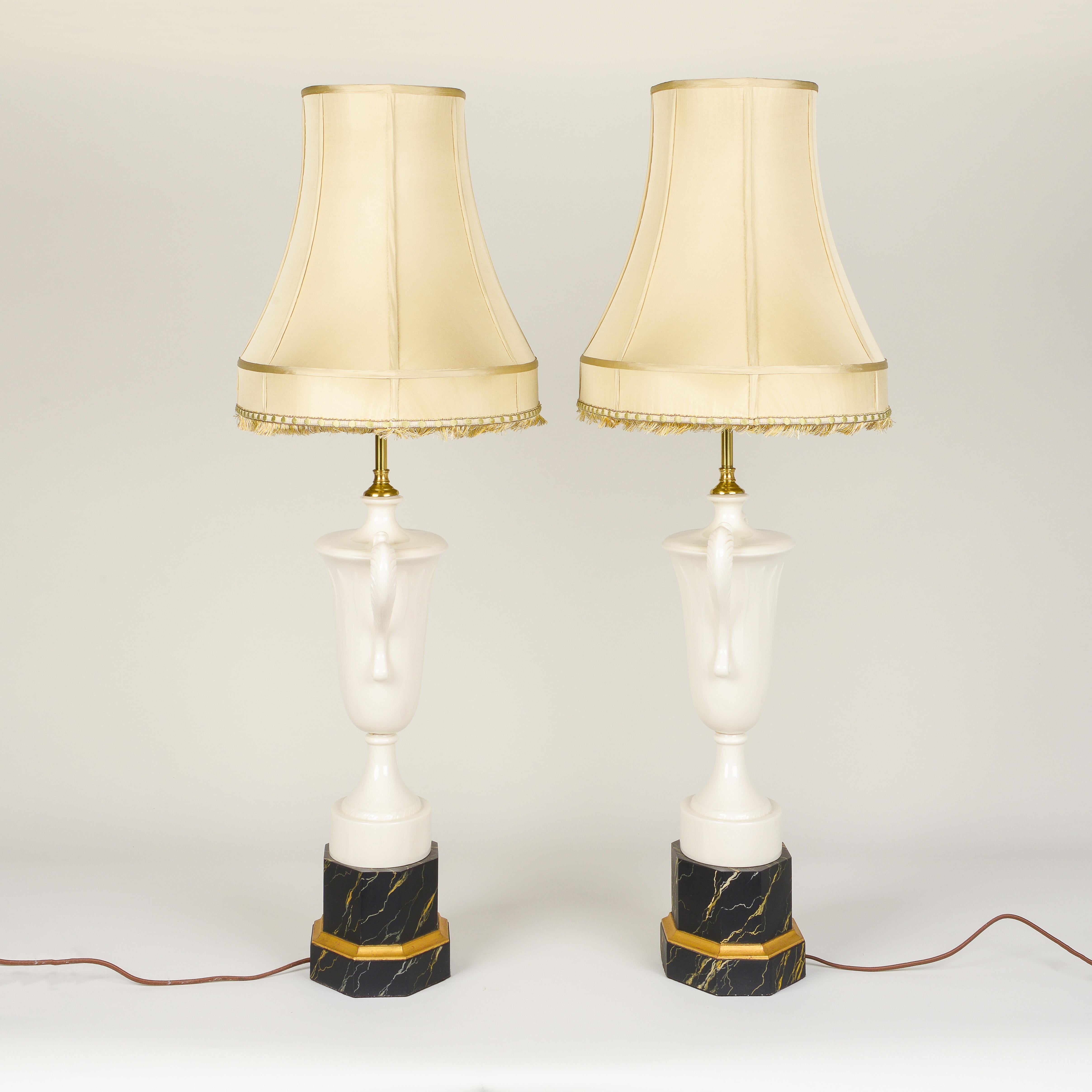 Each in the shape of a Grecian urn with two outward scrolling handles and fitted with two bulb sockets; mounted on black faux marble-painted bases with gilt banding. With pale gold silk shades.