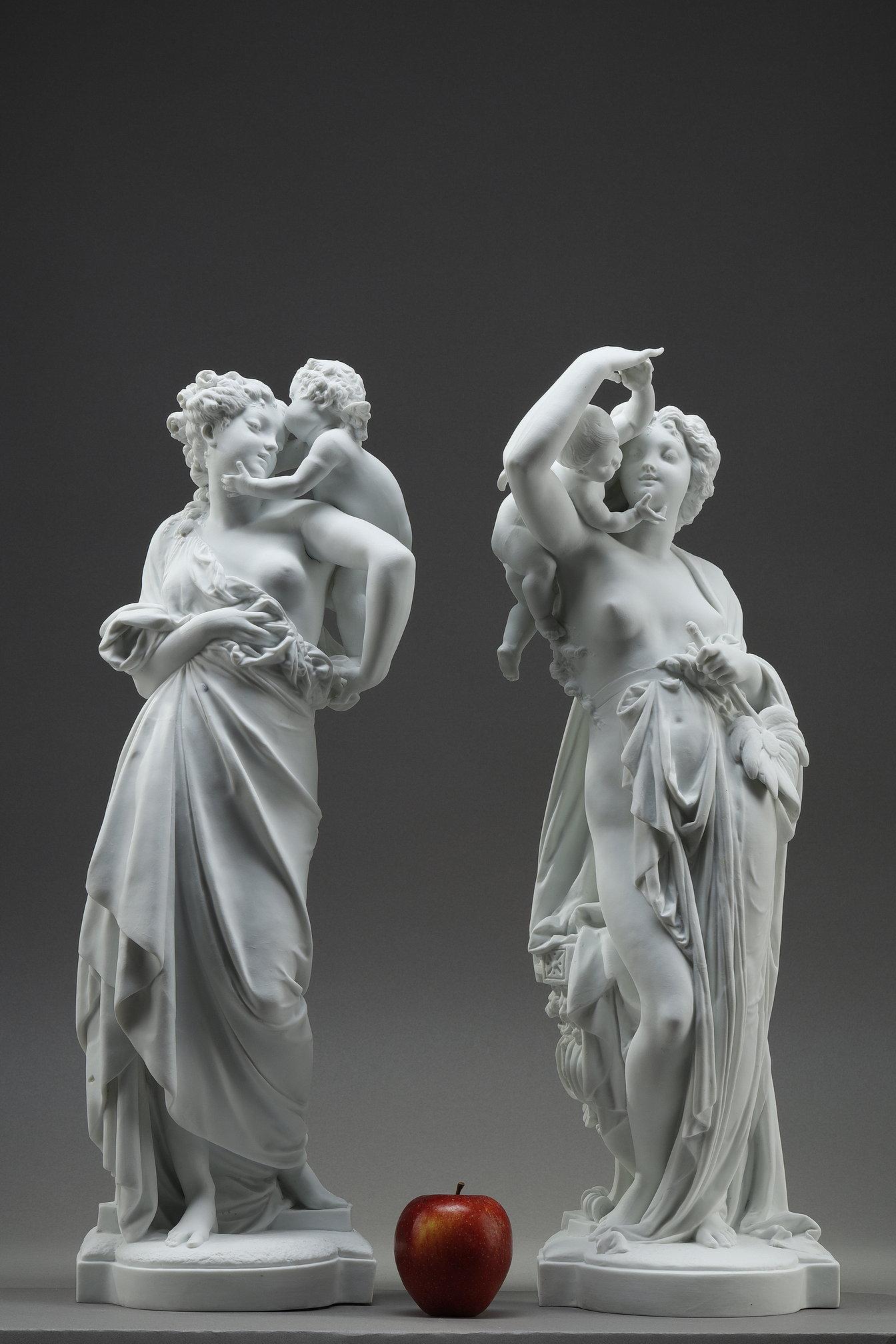 Importante coppia di sculture decorative in biscuit bianco, con due donne drappeggiate in stile antico, accompagnate da putti alati. Una, con in mano un grande girasole, alza il braccio in un gesto di svelamento, mentre il bambino la abbraccia.