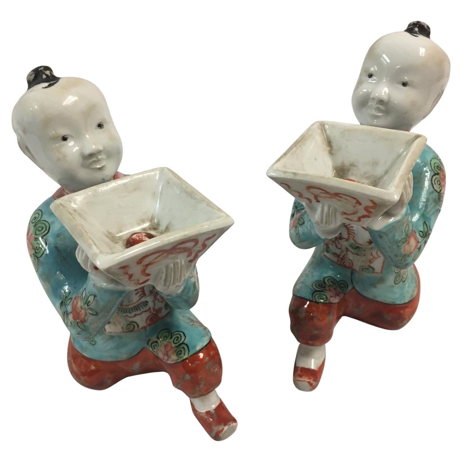 This whimsical pair of porcelain figures depict kneeling Chinese boys holding square containers suitable for single blossoms. The symmetry is graceful from all angles and the color palette is lovely. Features include a smooth glaze over hand painted