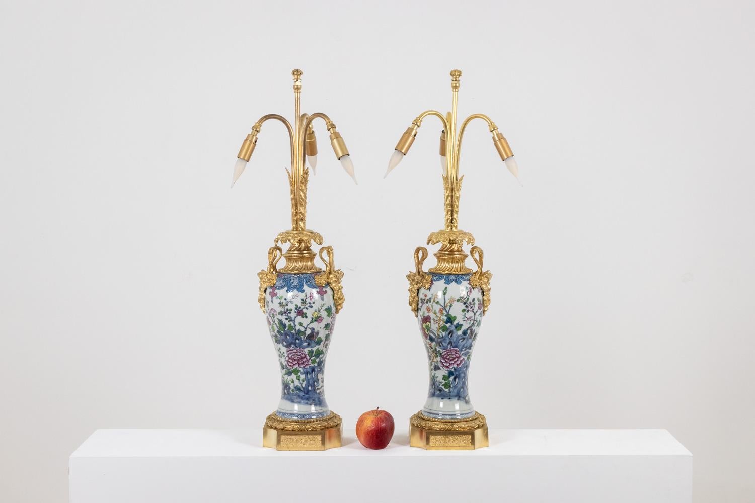Paire de lampes en porcelaine de Canton, dans les tons bleu et rose, décorées de pivoines. Base et monture en bronze doré, la monture dans sa partie centrale, aux anses finement incurvées, décorée de satyres et présentant un godron orné de bouquets